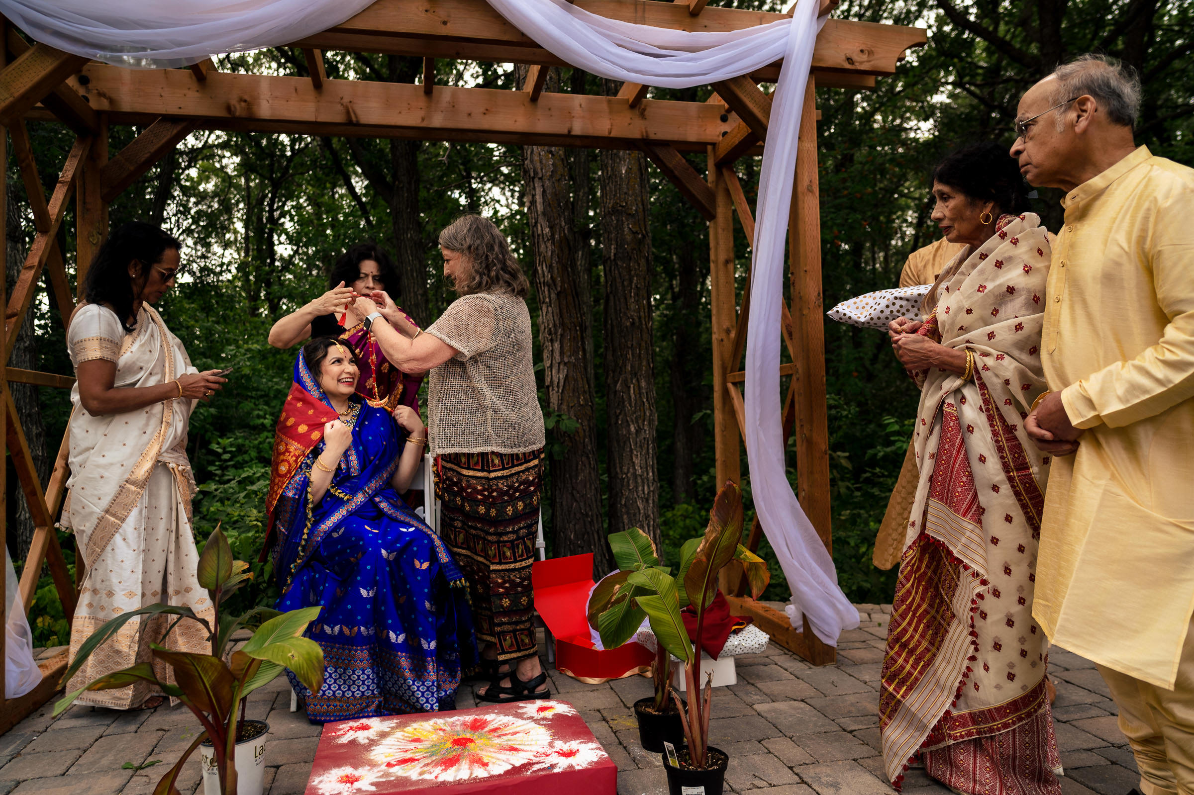 A woman is adorned in a colorful Winnipeg wedding under a wooden arbor outdoors.