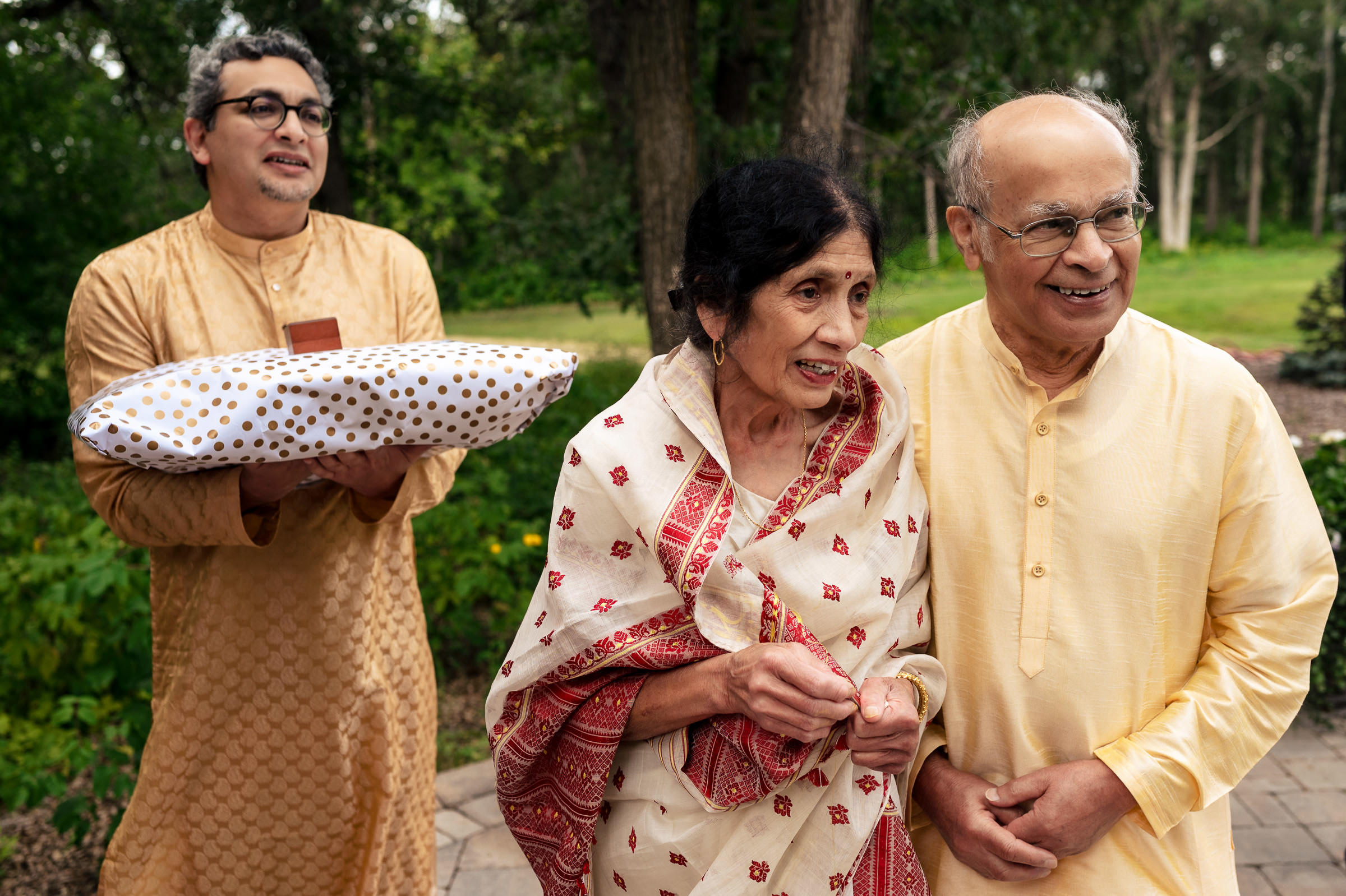 Three people in traditional attire at a Winnipeg wedding, one with a decorated pillow.