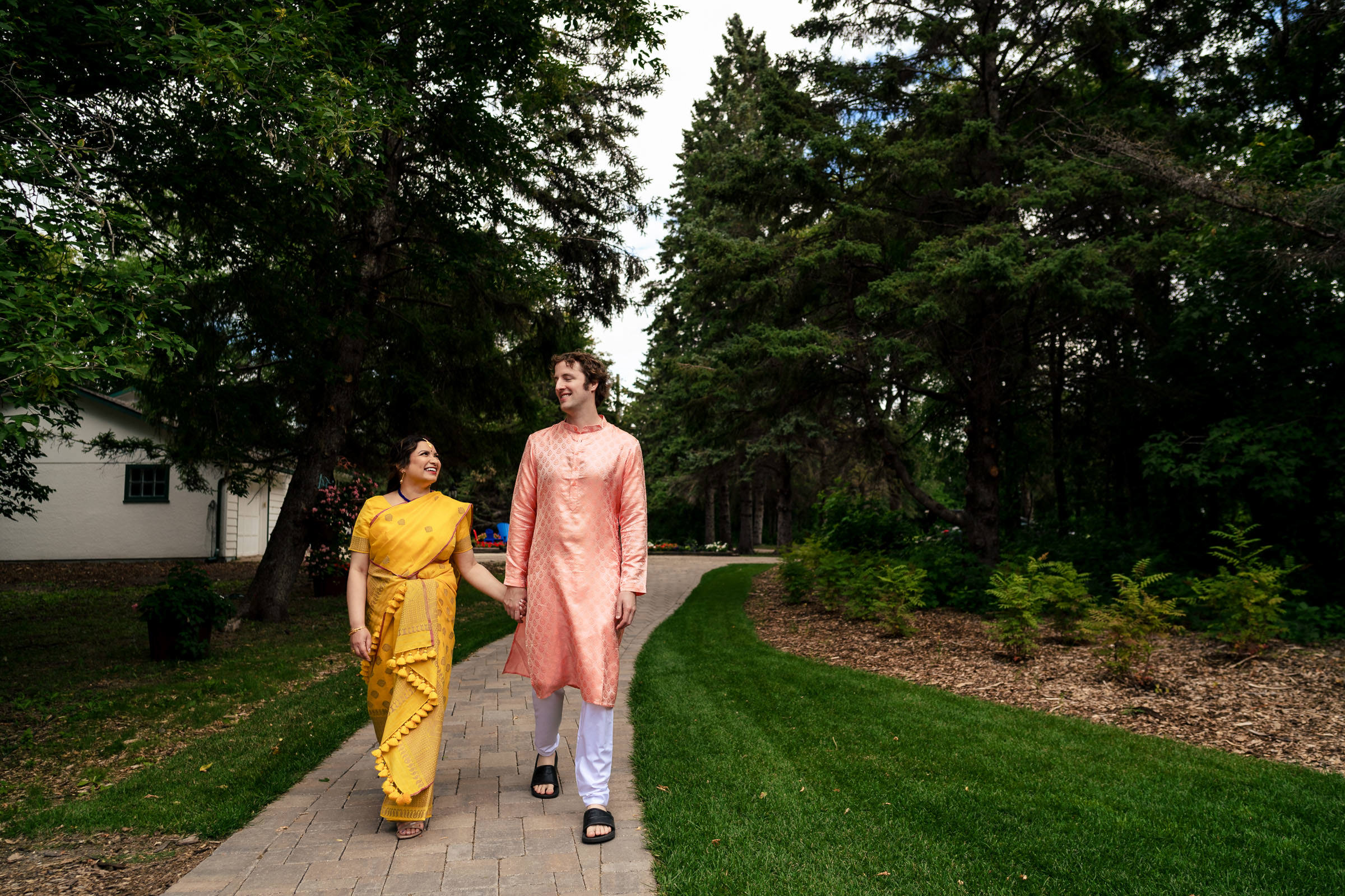 A couple in traditional attire strolls a paved path at a Winnipeg wedding.