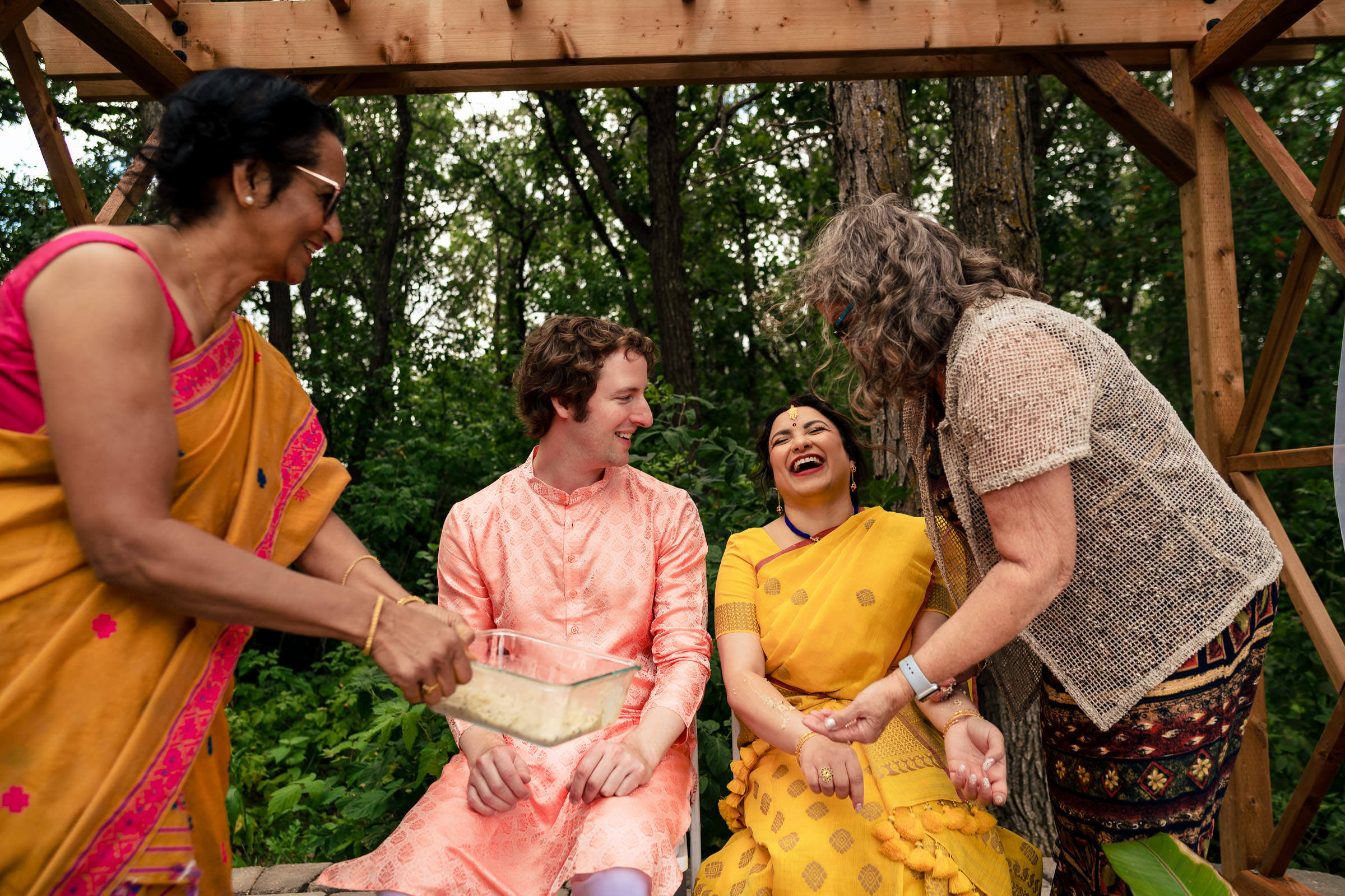 People laughing joyfully at a Winnipeg wedding with trees swaying in the background.
