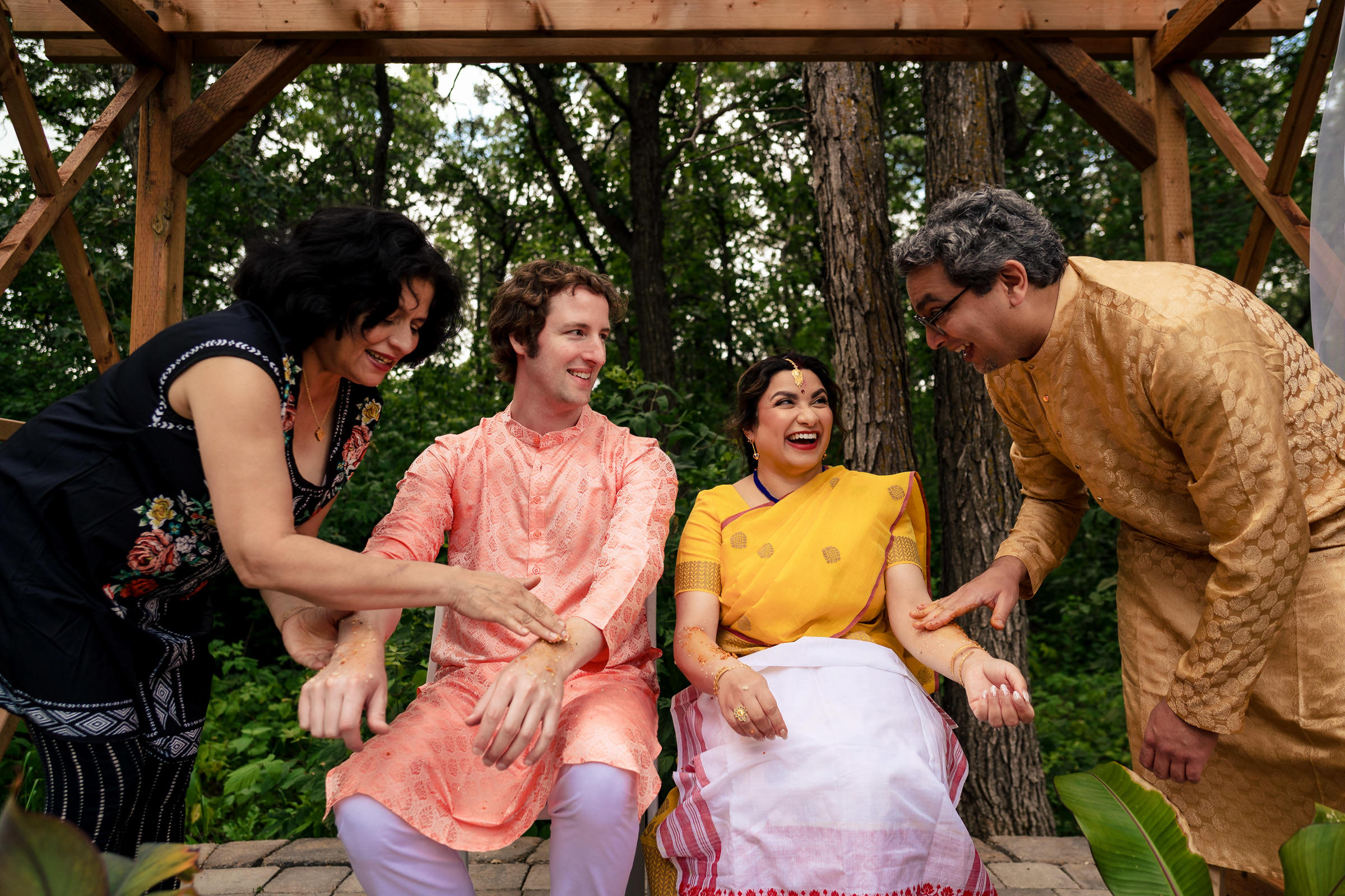 A Winnipeg wedding with four laughing guests applying turmeric to the couple in the woods.