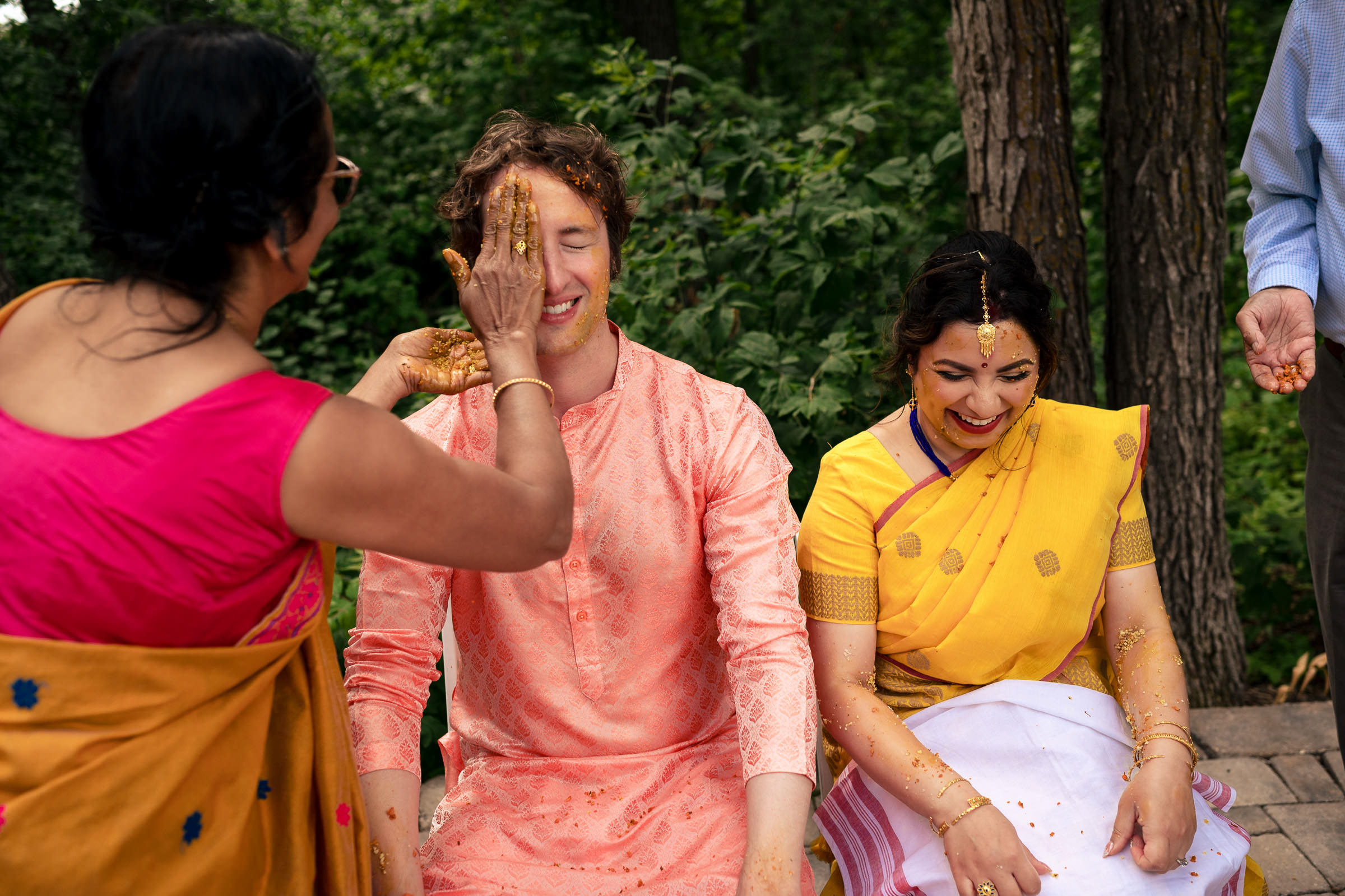 Two people in colorful clothing enjoy a Winnipeg wedding, one applying paint to the other.