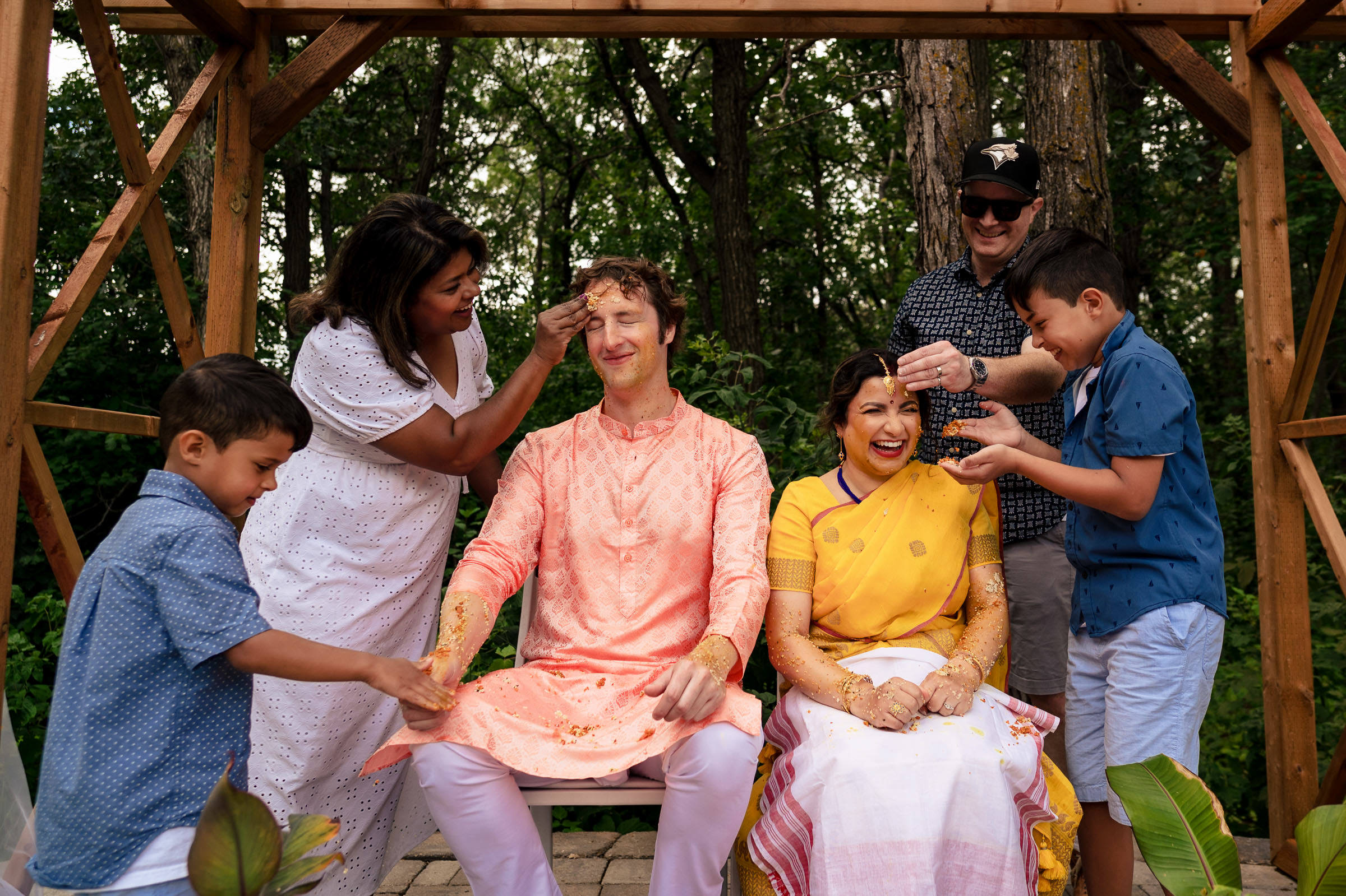 A couple smeared with turmeric at an outdoor Winnipeg wedding, surrounded by four people.