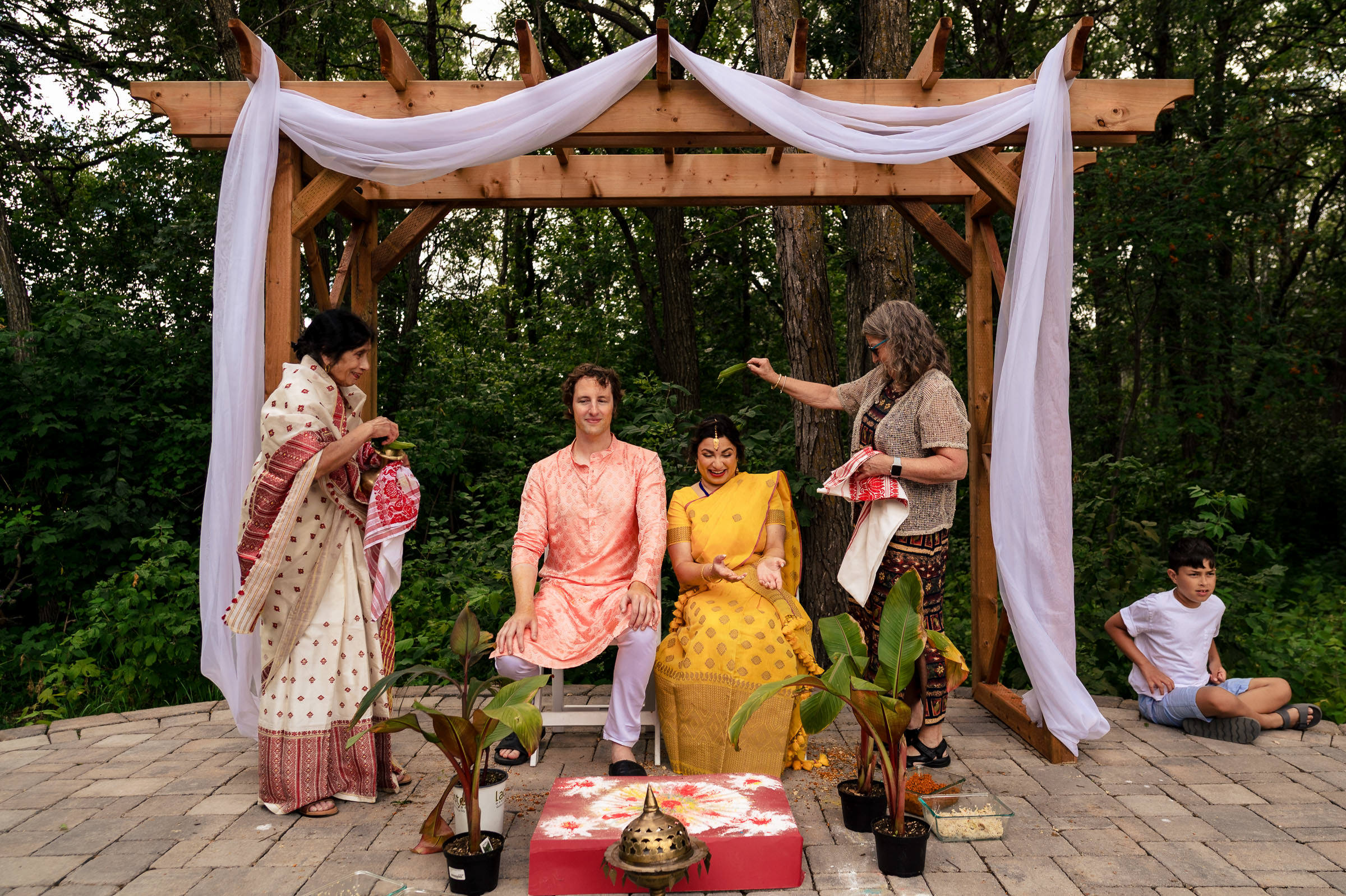 Guests in traditional attire gather at a Winnipeg wedding under a wooden canopy with white cloth.