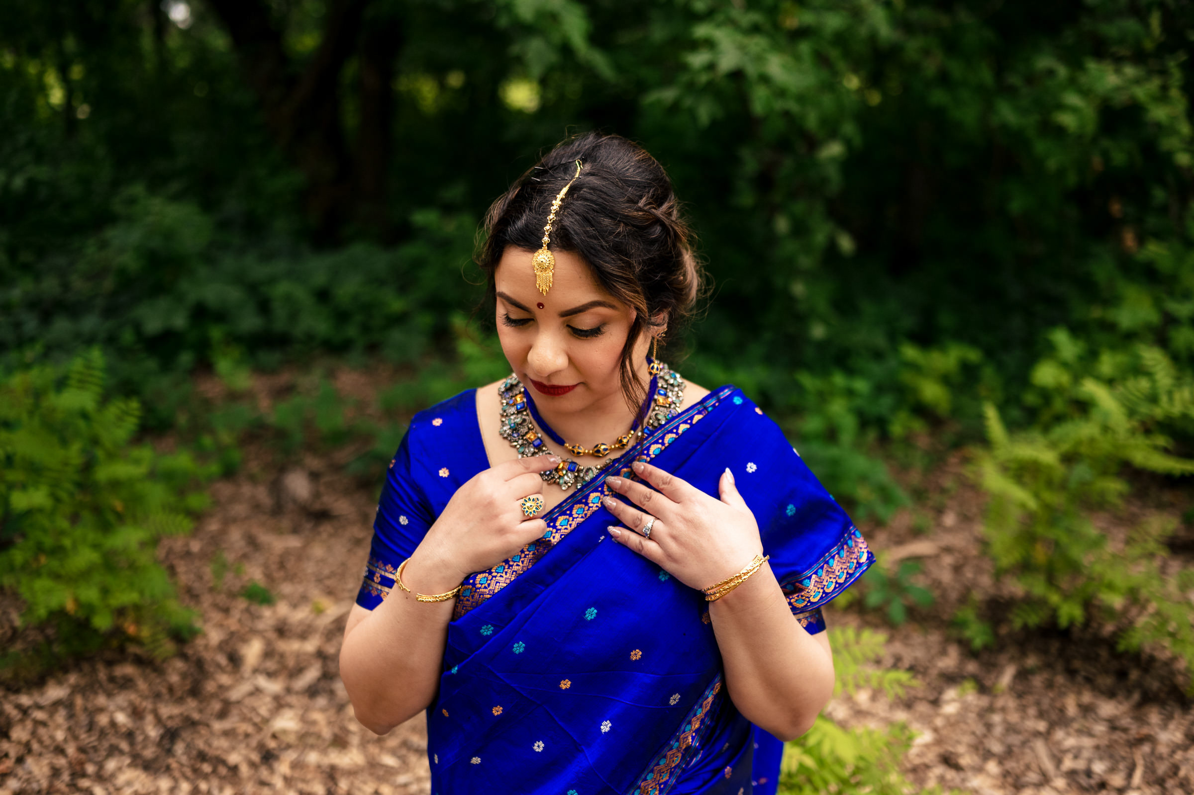 A woman in a blue sari with gold jewelry stands outdoors at a Winnipeg wedding.