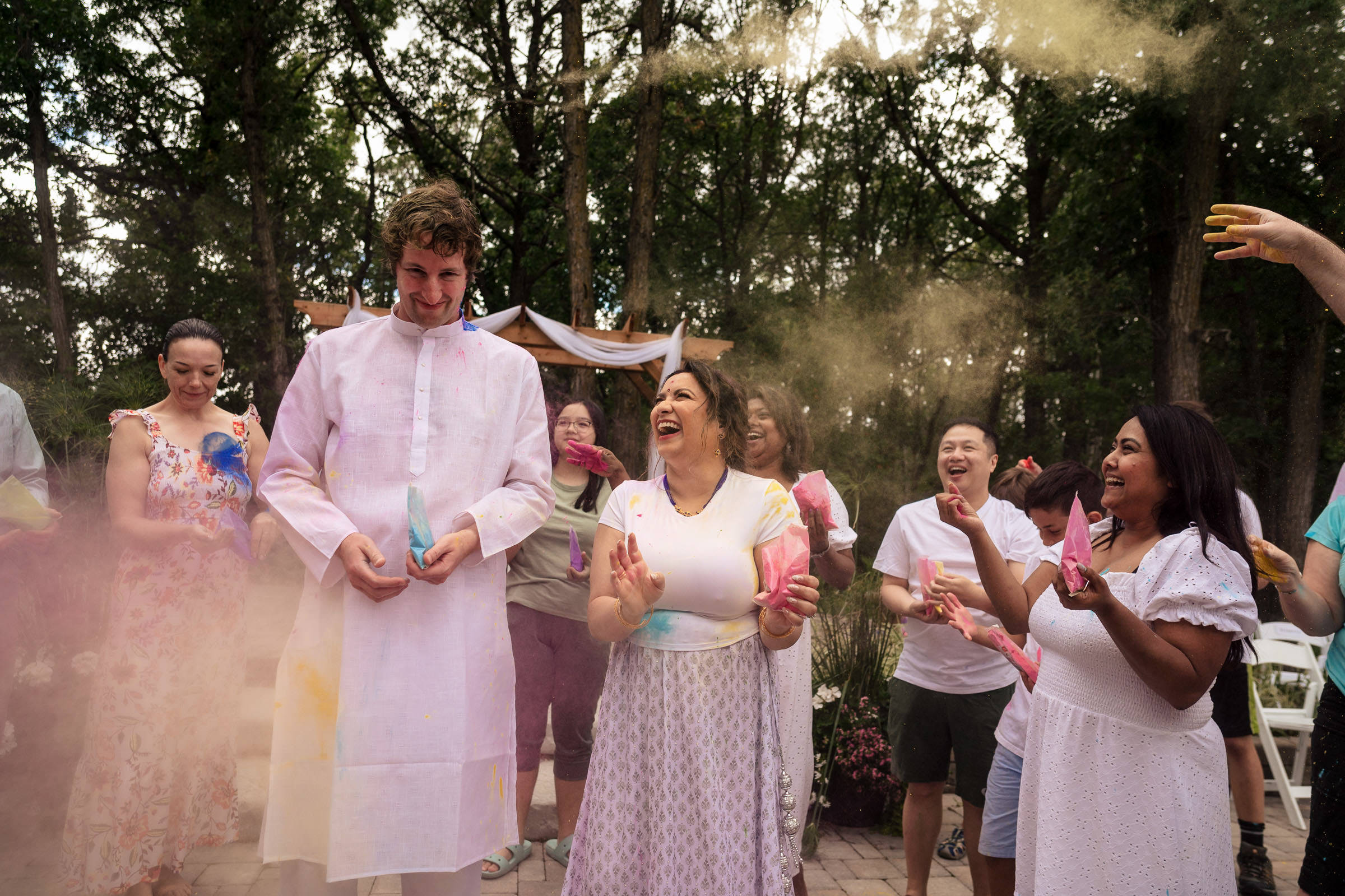 People celebrating outdoors with colorful powder, in festive attire like a Winnipeg wedding.