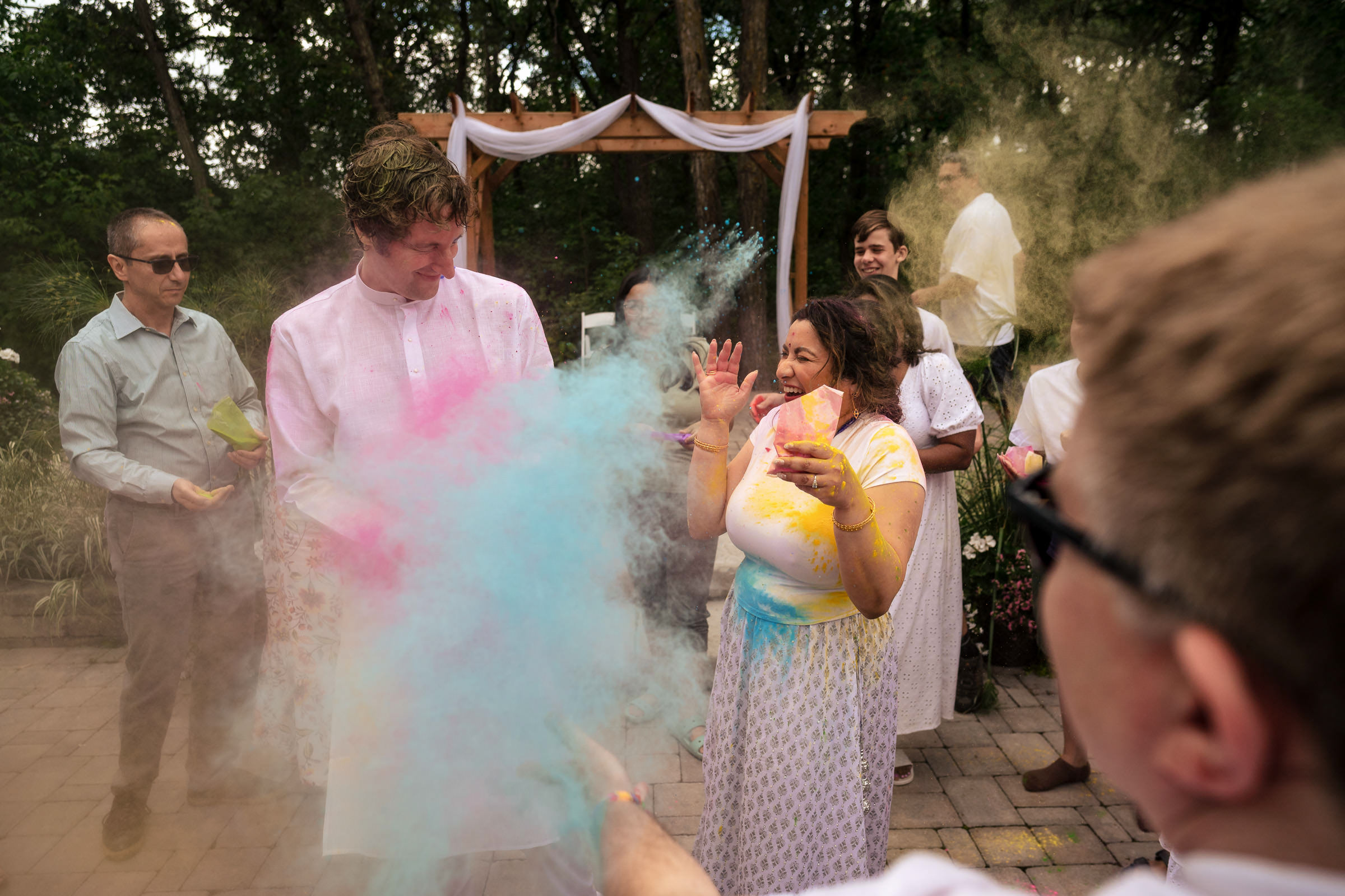 Winnipeg wedding guests celebrating with colored powder outdoors in light clothing.