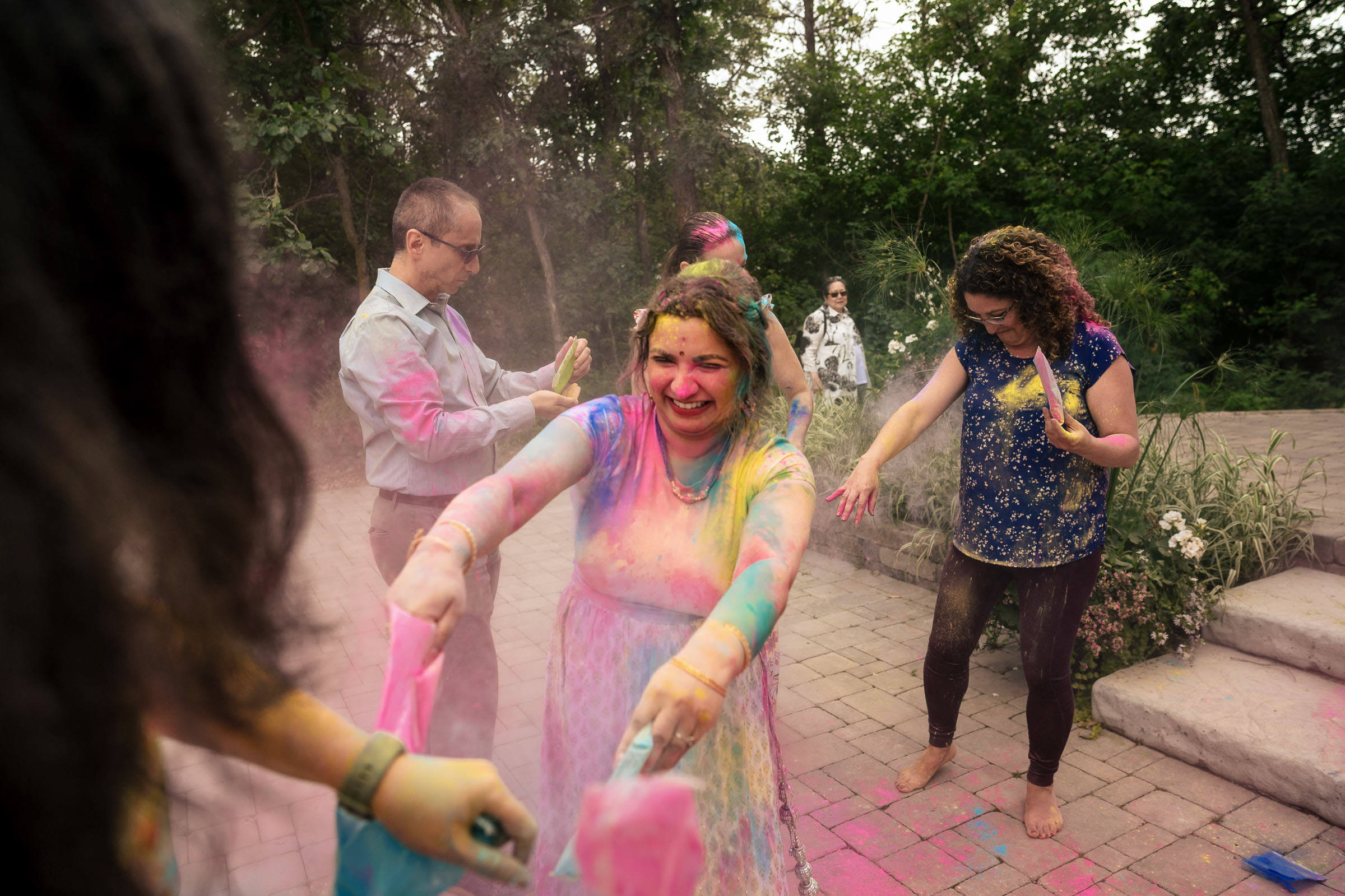 A Winnipeg wedding with people celebrating in colorful powder under the trees.