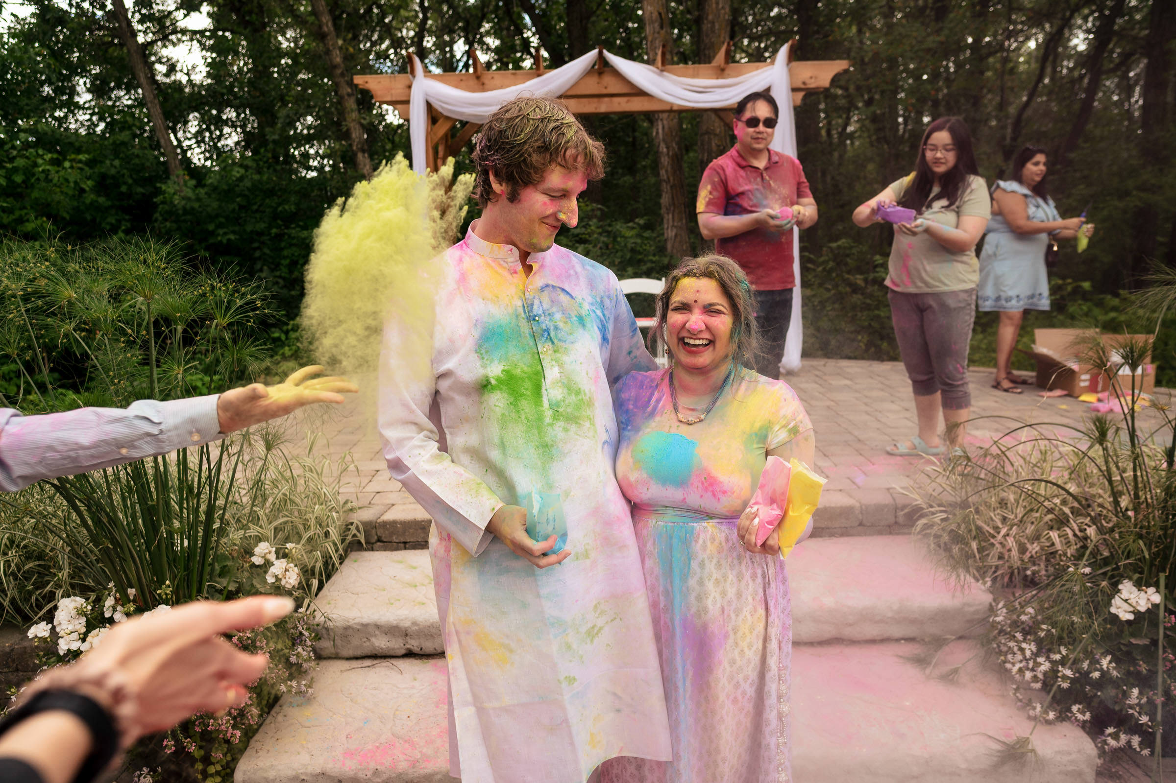 A couple smiles in colorful powders at a lively Winnipeg wedding celebration.