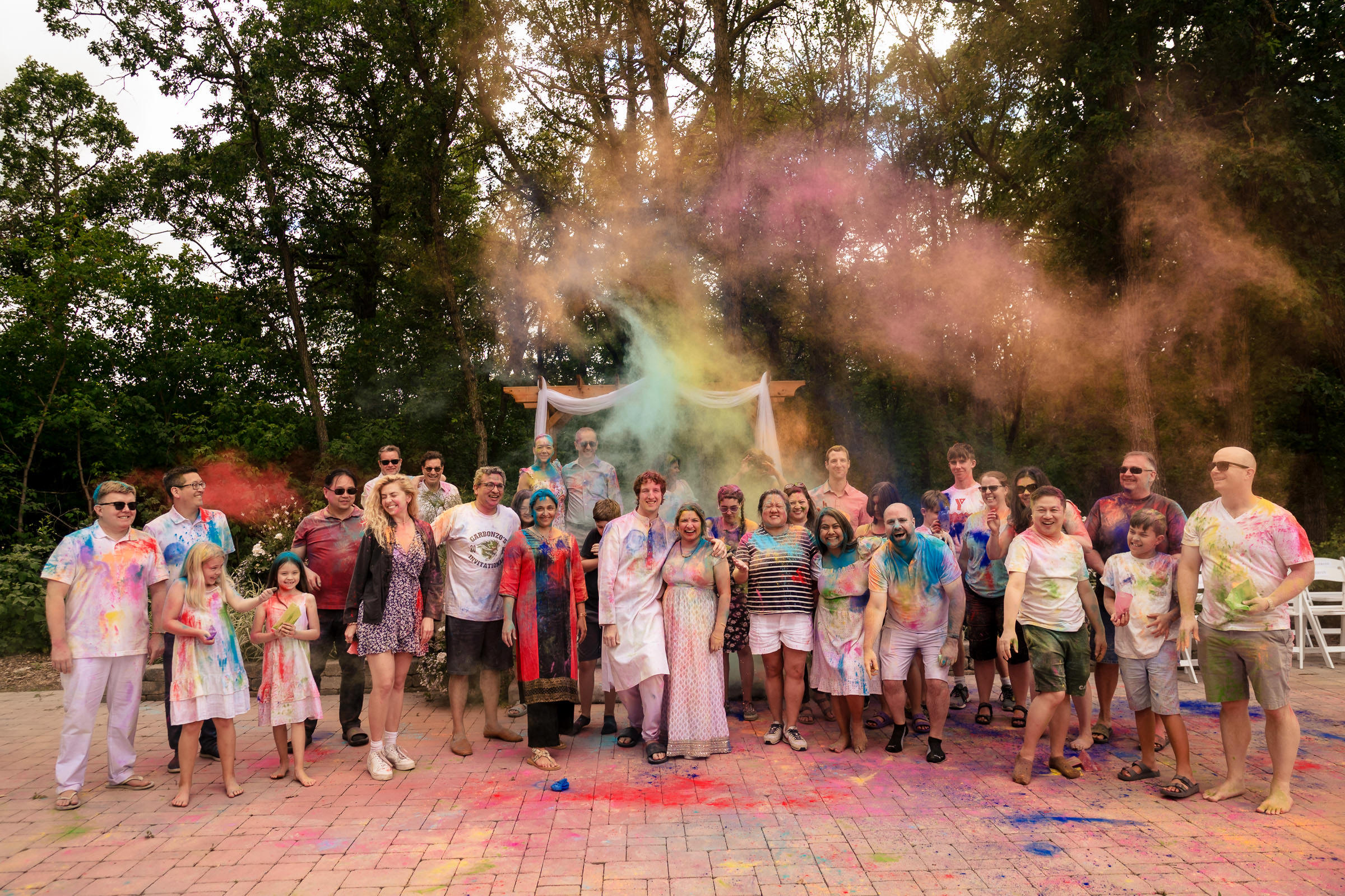 Group celebrating with colorful powder outdoors at a Winnipeg wedding, surrounded by trees.