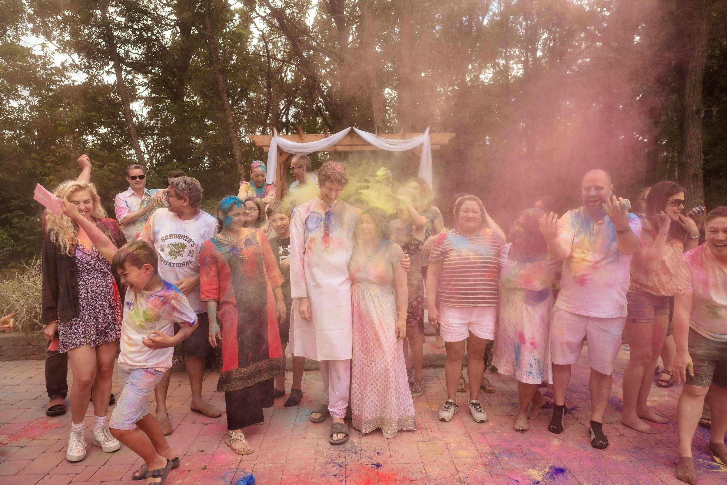 Group of people celebrating with colorful powder at a Winnipeg wedding outdoors.