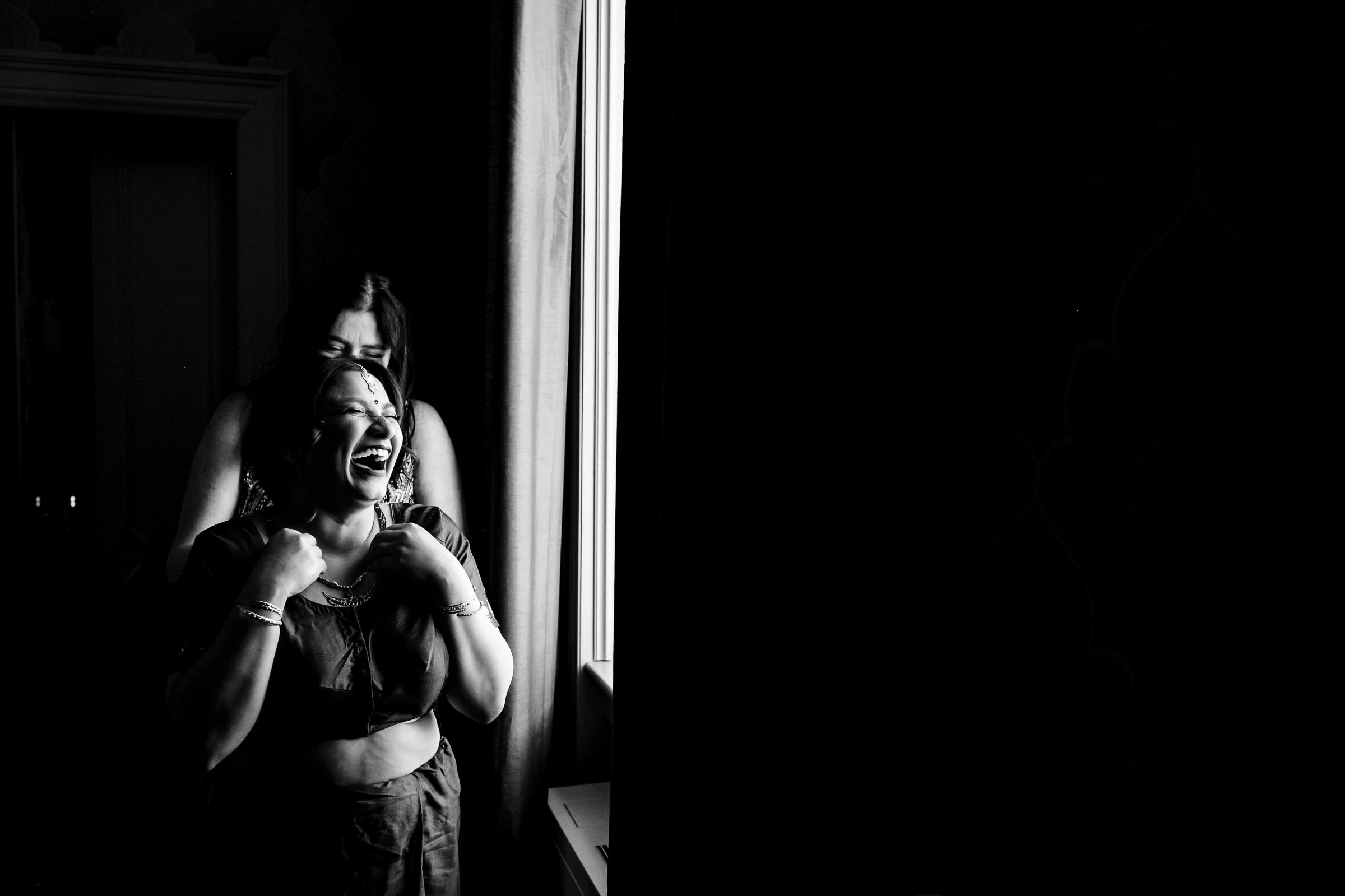 A Winnipeg wedding moment: two people by a window, one smiling widely, in black and white.