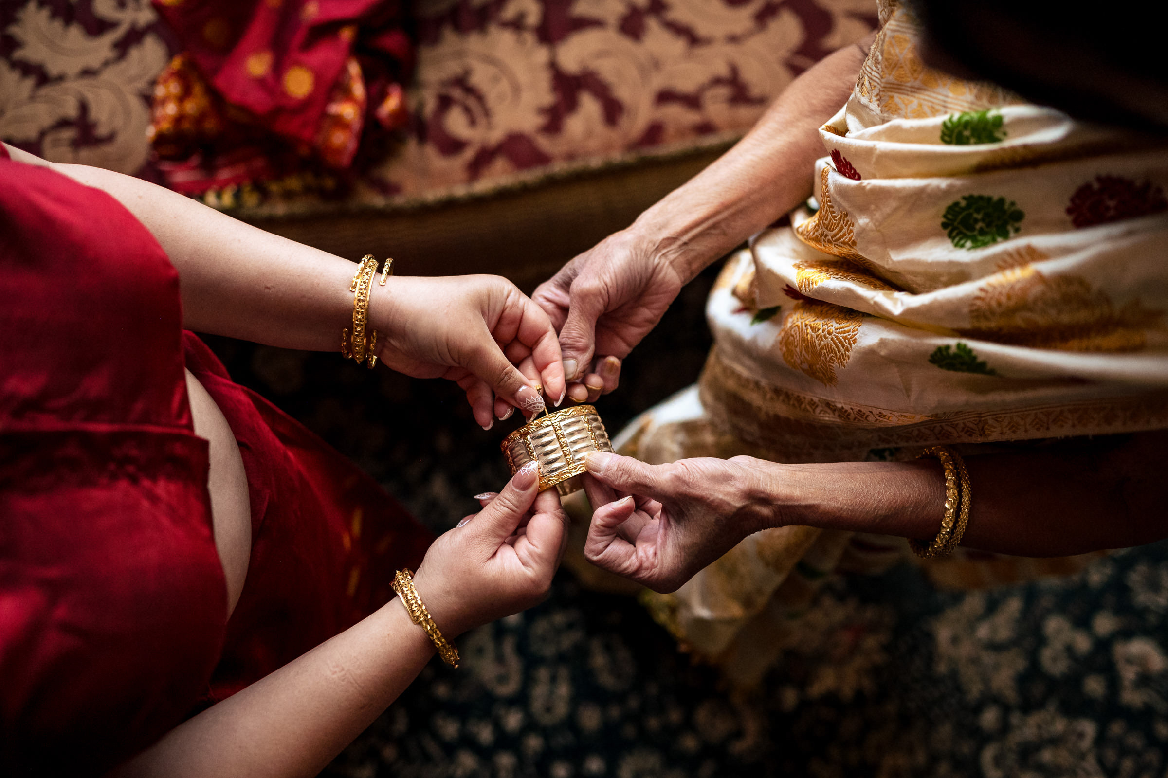 Two people at a Winnipeg wedding exchanging a gold bracelet, wearing patterned traditional attire.
