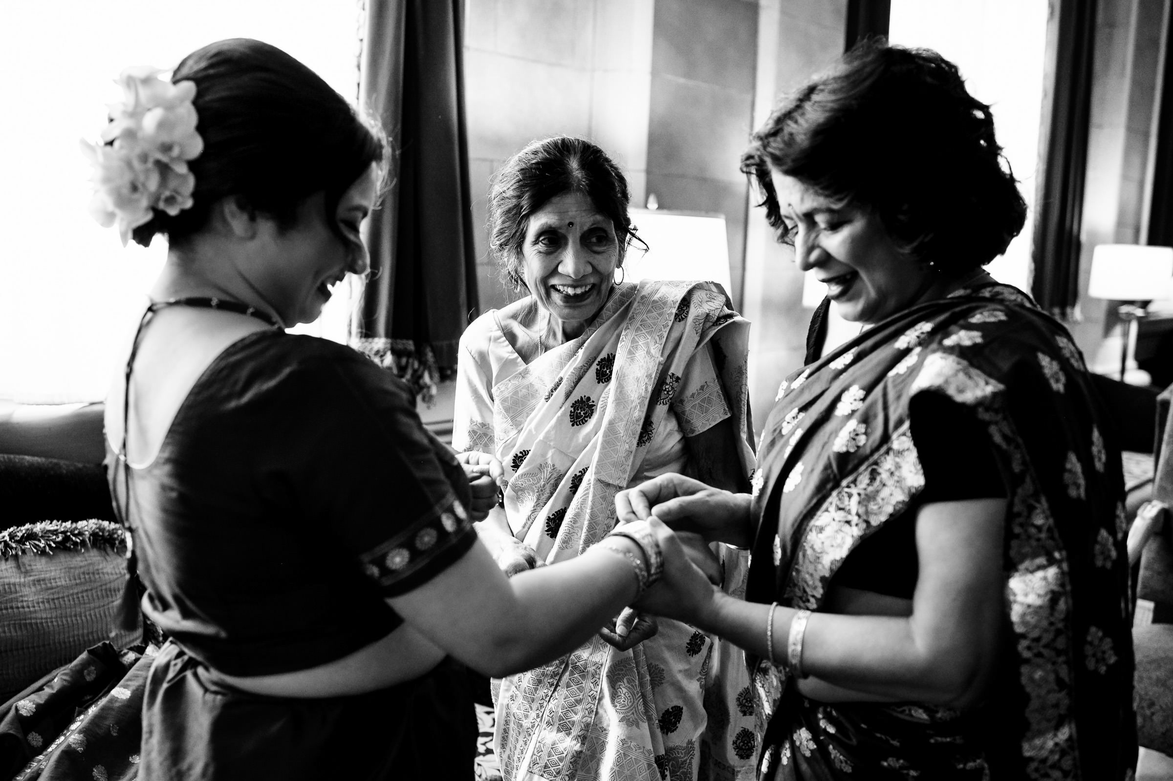 Three women in saris engage as light streams through a window at a Winnipeg wedding.