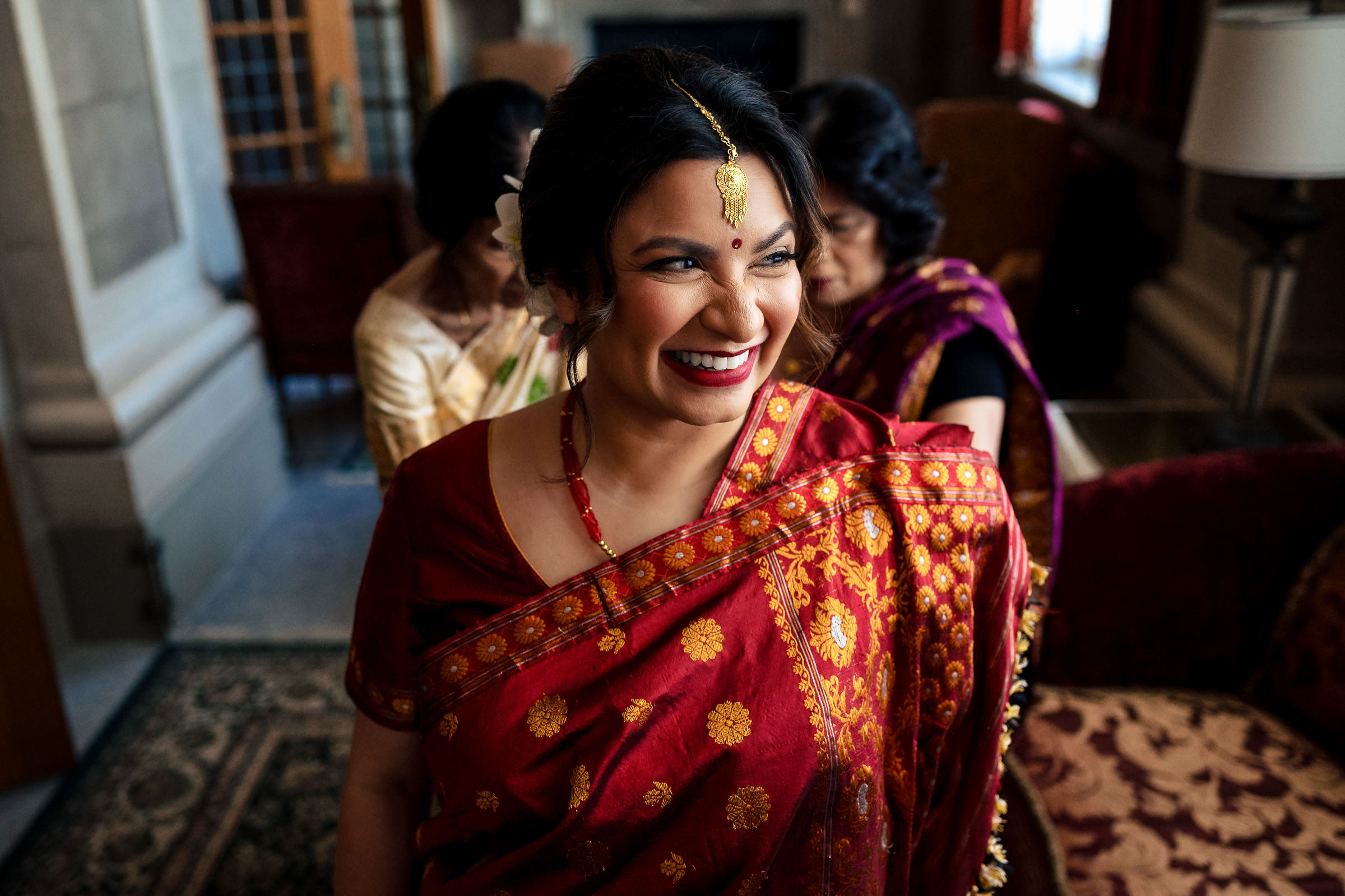 A smiling person in a red sari with gold details at an indoor Winnipeg wedding.