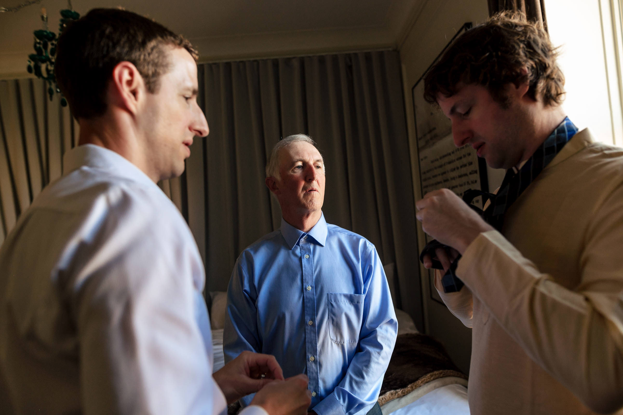 Three men in a room, two adjusting ties while the third looks on at a Winnipeg wedding.