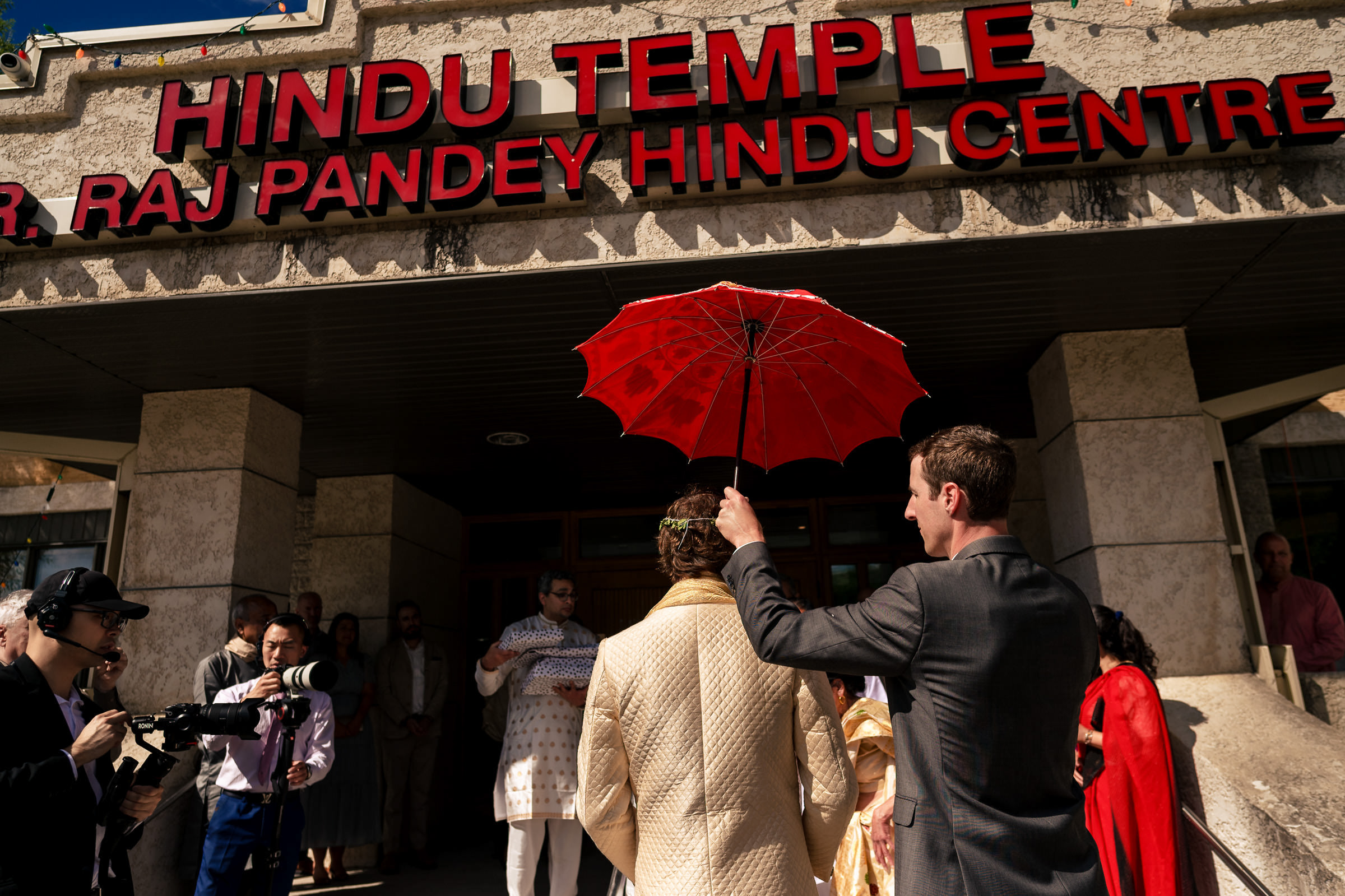 A group enters a Hindu temple, akin to a Winnipeg wedding scene, one with a red umbrella.