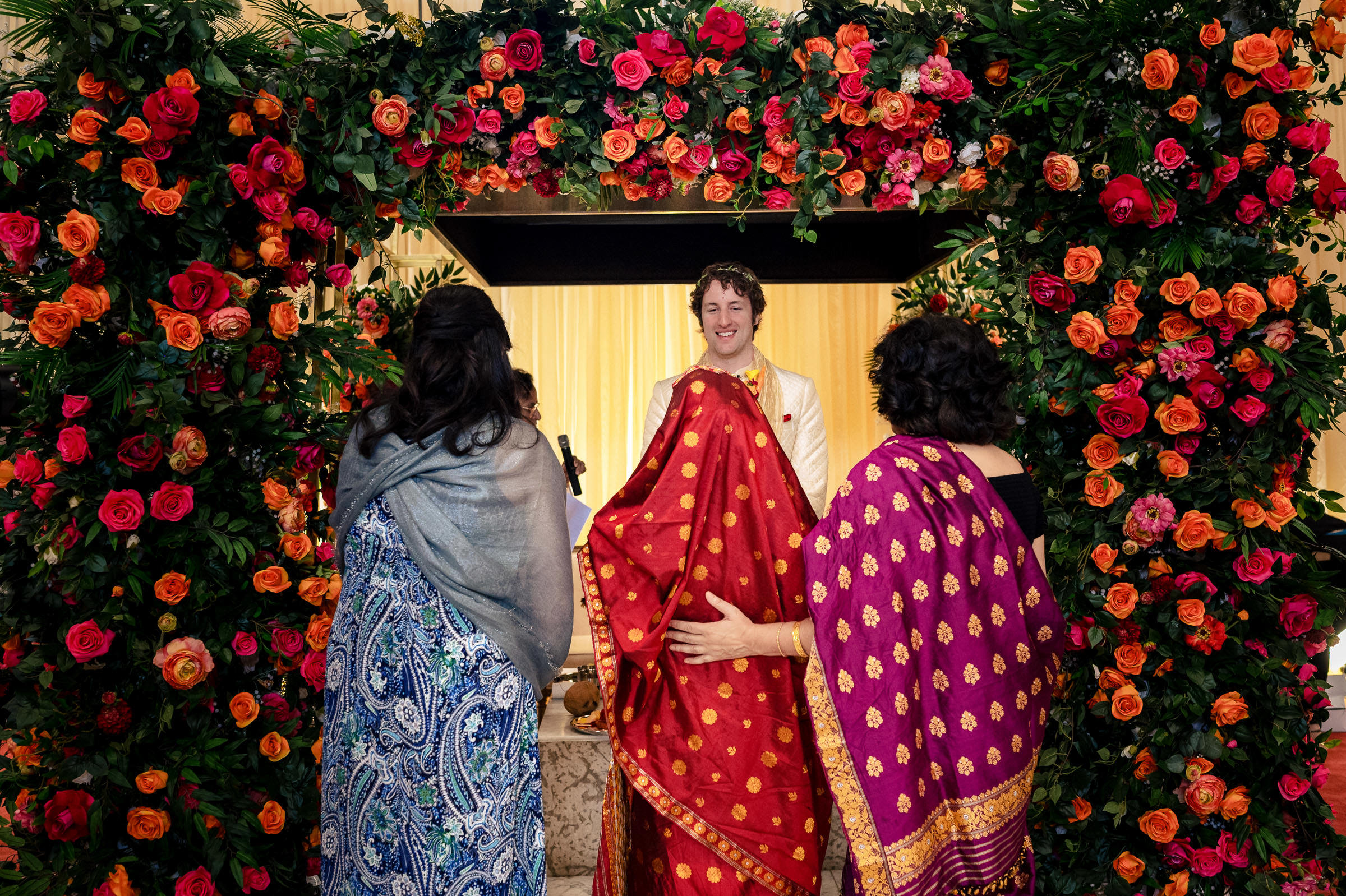A man smiles at two women with colorful fabric in a Winnipeg wedding setting.
