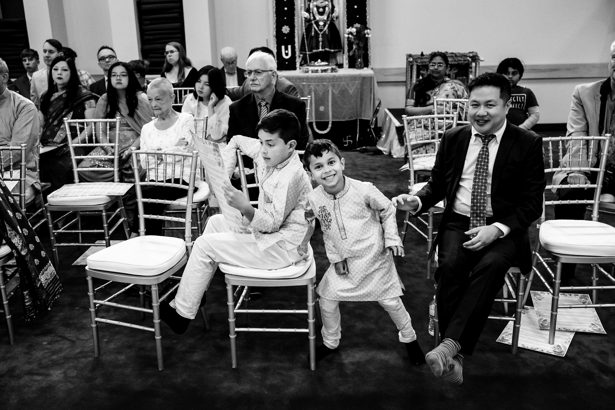 Children playing on chairs at a Winnipeg wedding, with adults observing in the background.