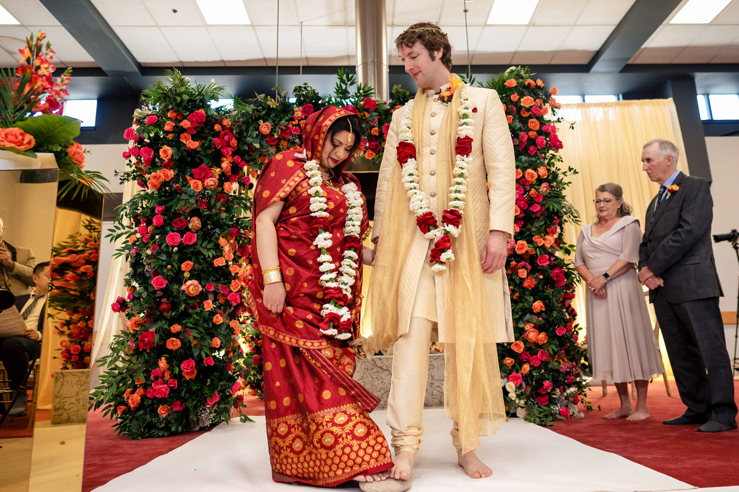 A couple in traditional attire poses before a floral backdrop at their Winnipeg wedding.