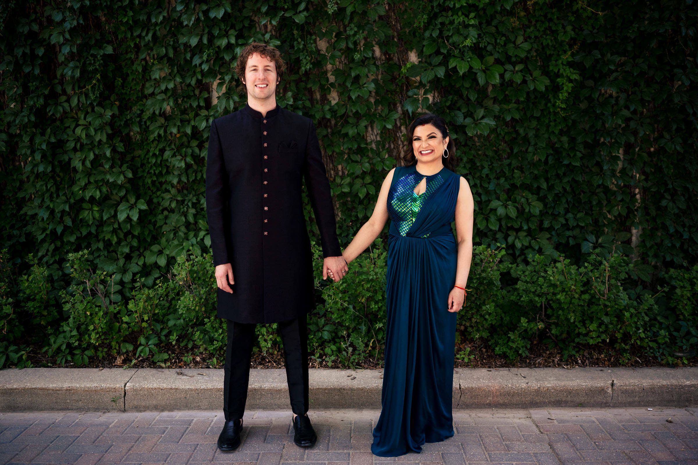 A couple stands holding hands at a leafy wall, capturing their Winnipeg wedding bliss.