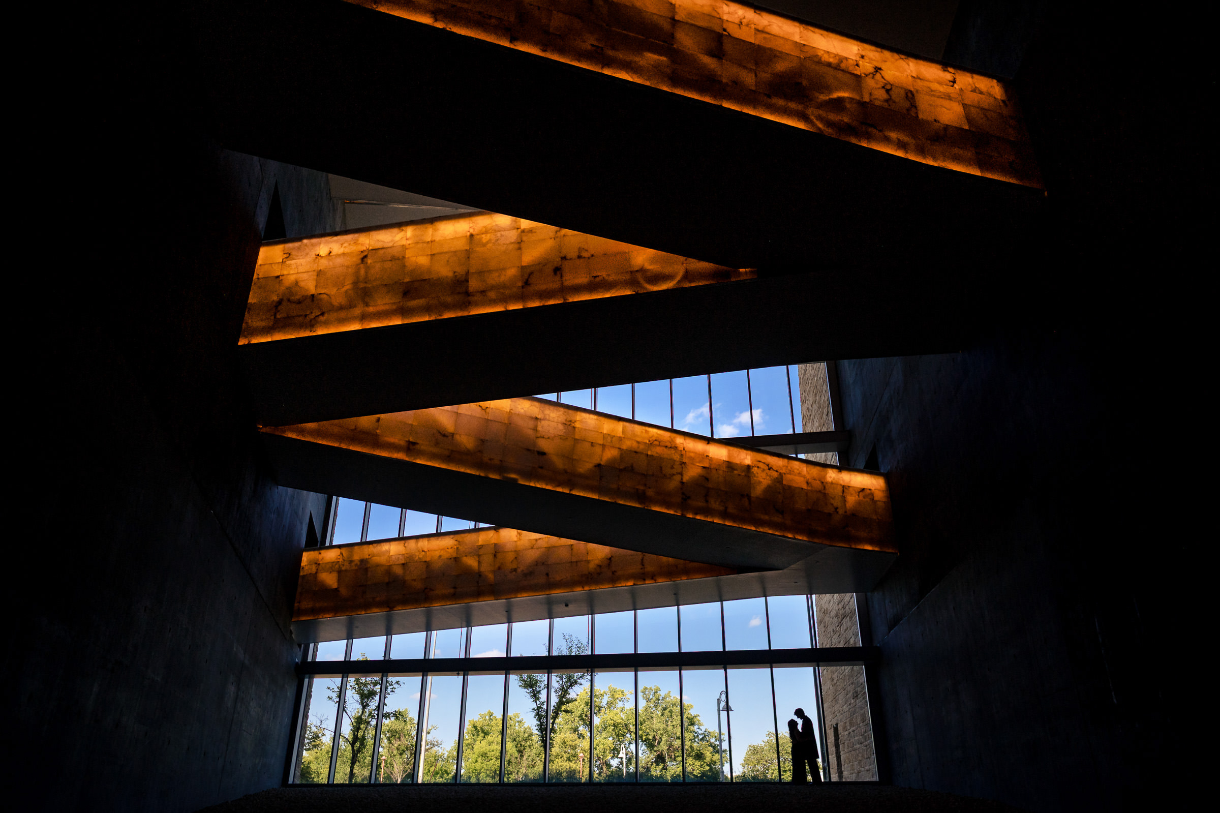 Silhouetted person in dark room, large windows showing trees; a serene Winnipeg wedding scene.