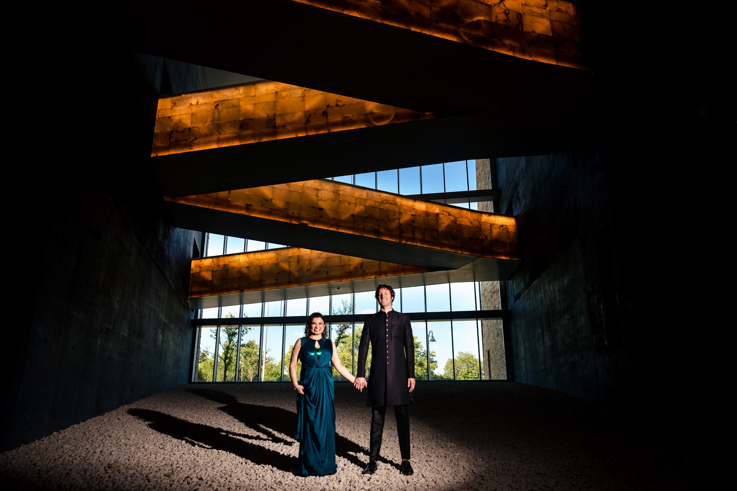 A couple holds hands in a modern Winnipeg wedding venue with angled lights and large windows.