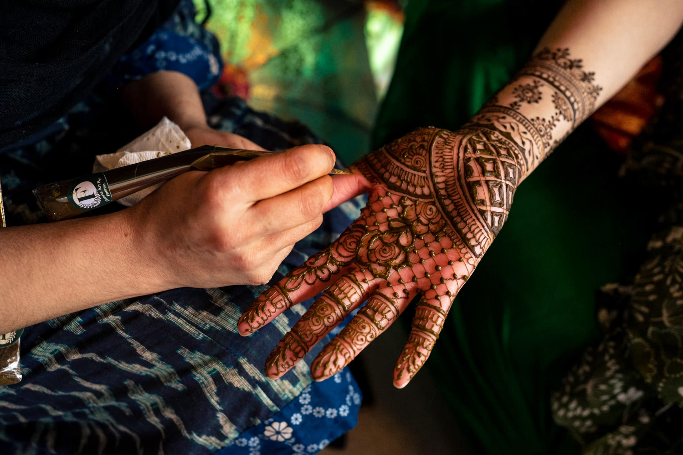 Hand being decorated with intricate henna designs.