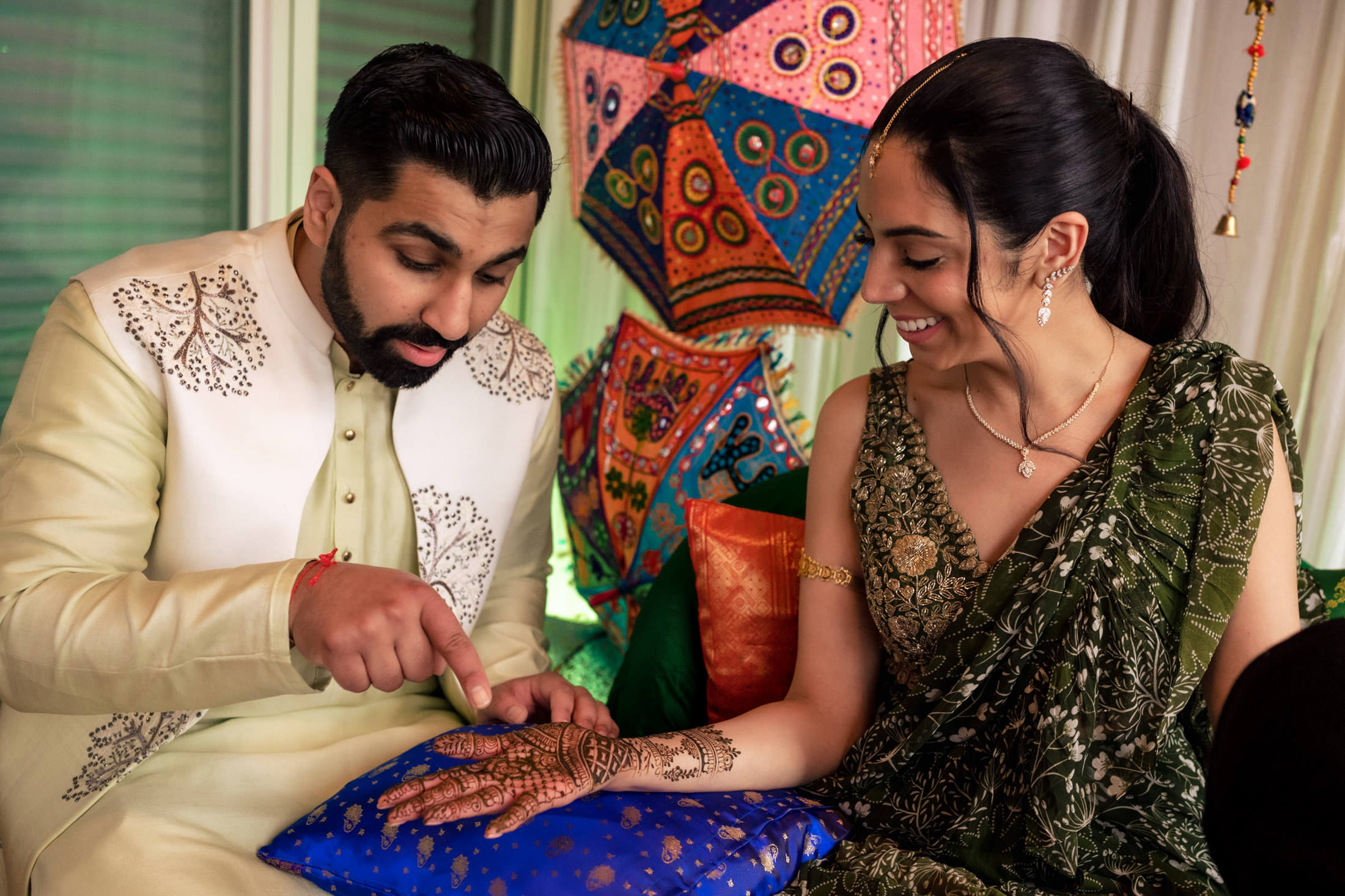 Couple enjoying a Mehndi ceremony with colorful umbrellas in the background.