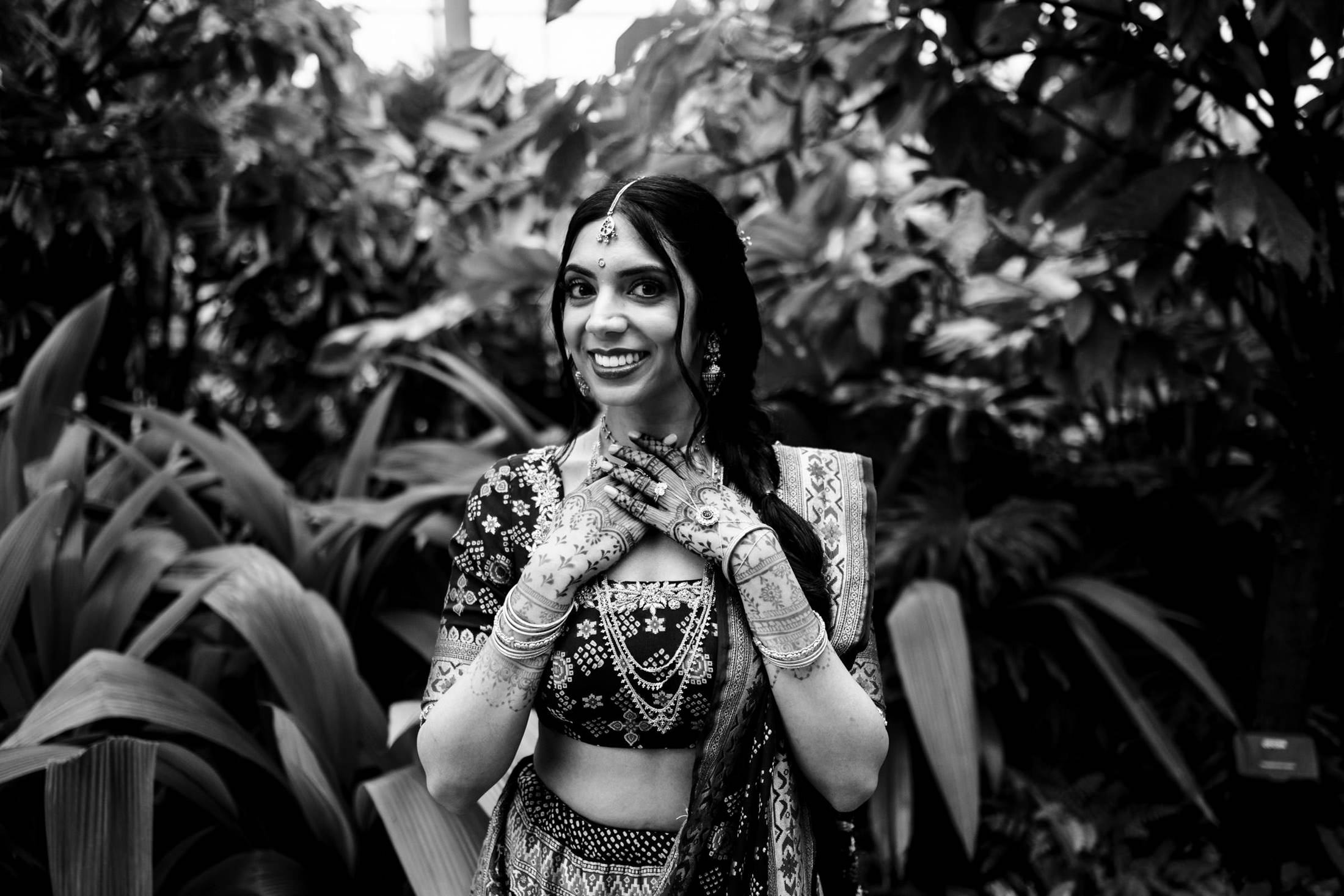 Woman in traditional attire with henna, smiling amidst lush greenery.