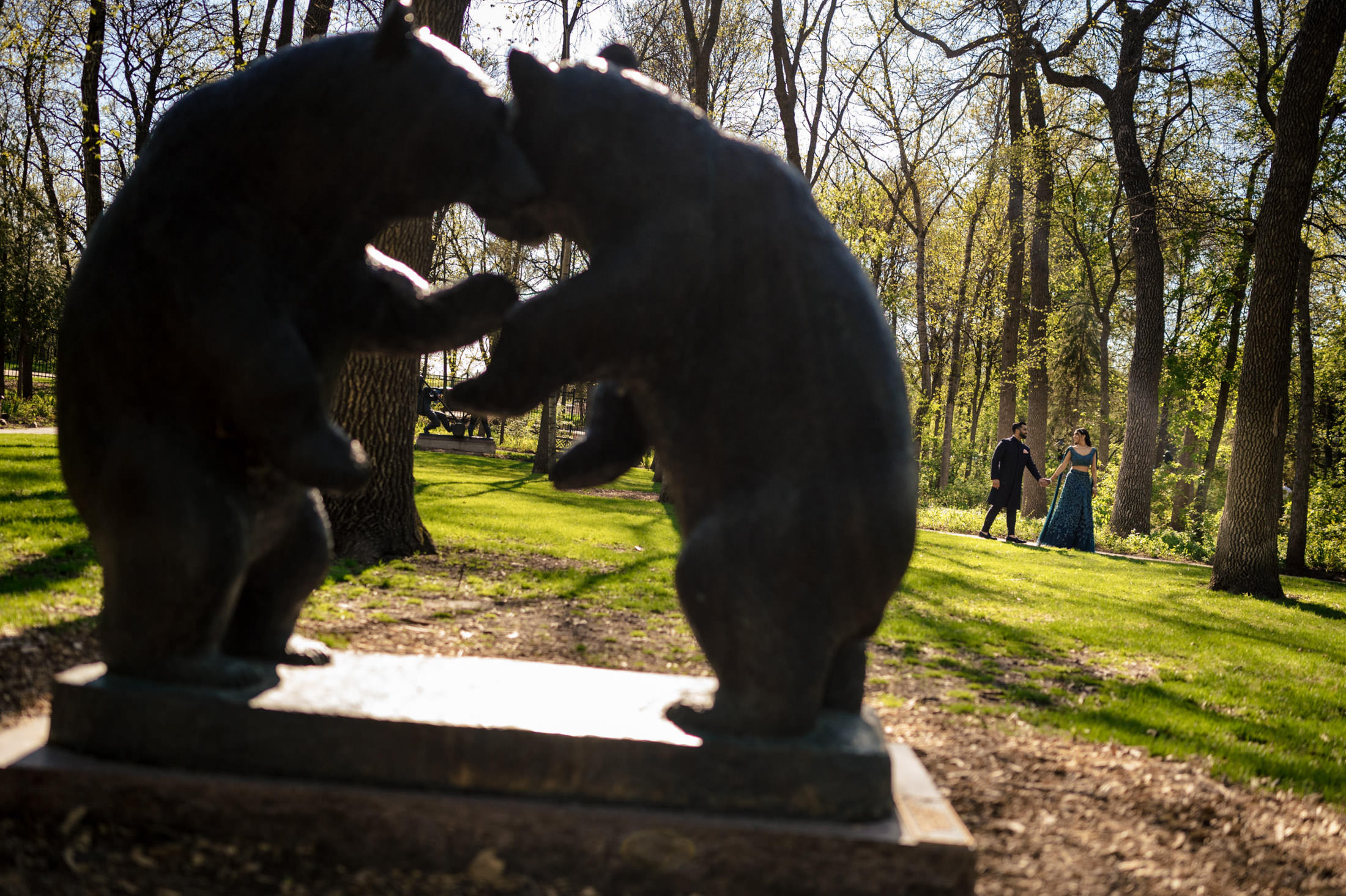 Bear statues facing each other; couple walking in a sunlit forest clearing.