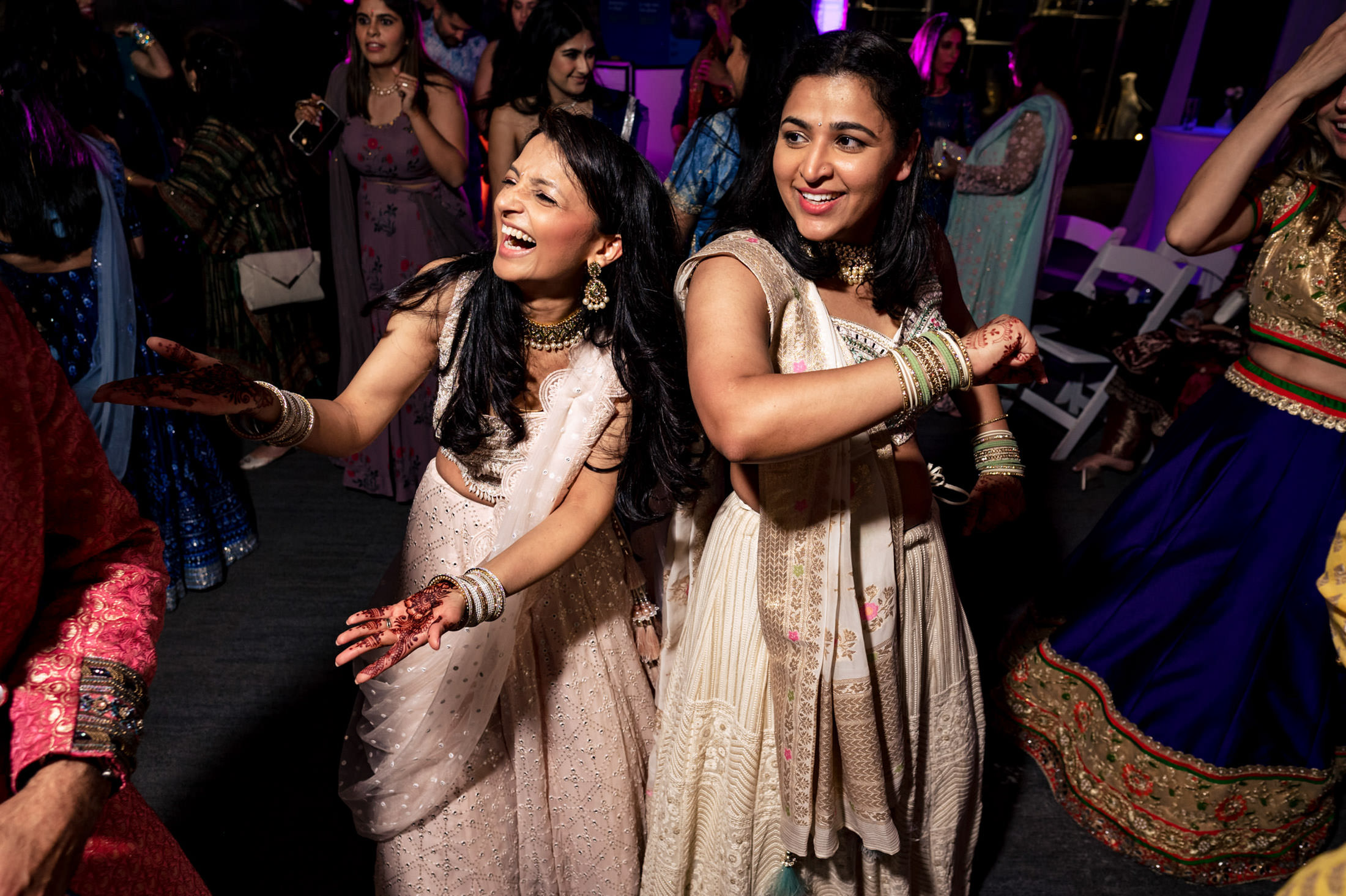 Two women in elegant traditional attire dancing joyfully at a vibrant celebration.