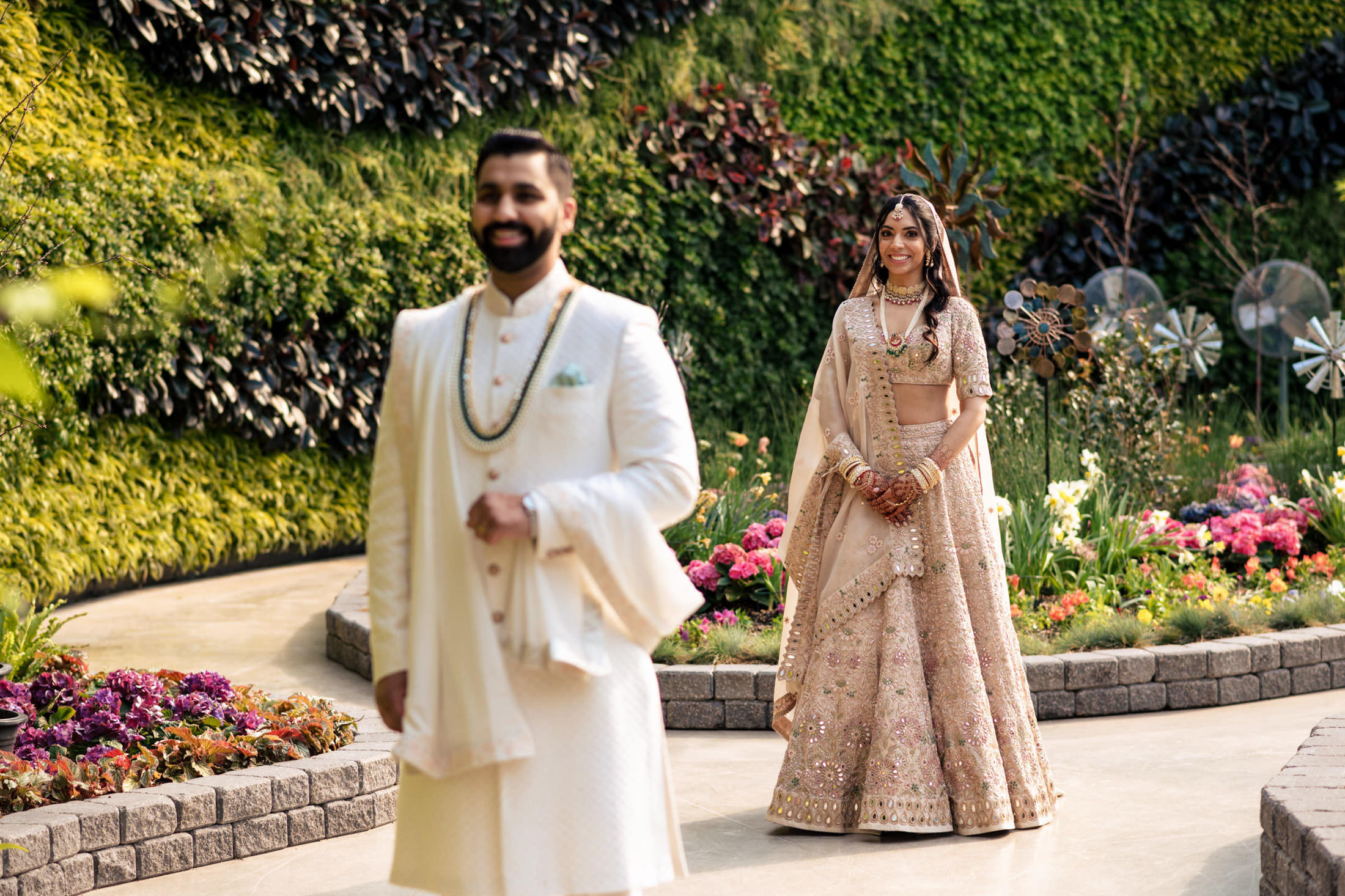 A bride and groom in traditional attire walking in a garden.