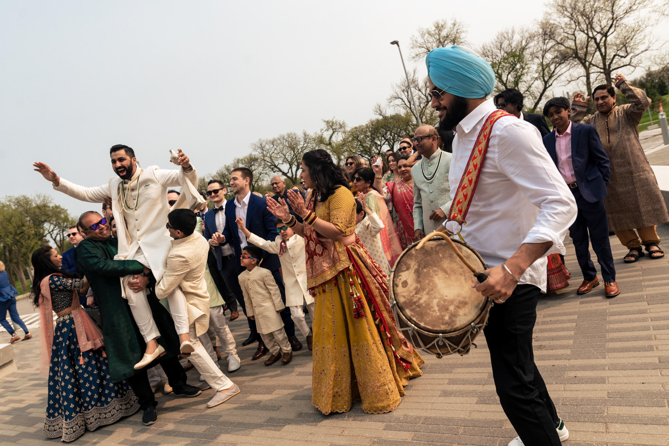 Group celebrating with music and dance, person lifted joyfully, drummer leading.