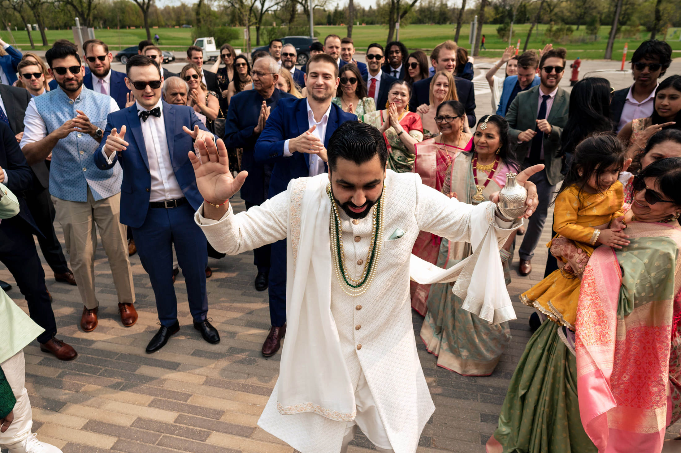 A joyful groom dances in front of a cheering crowd at an outdoor celebration.