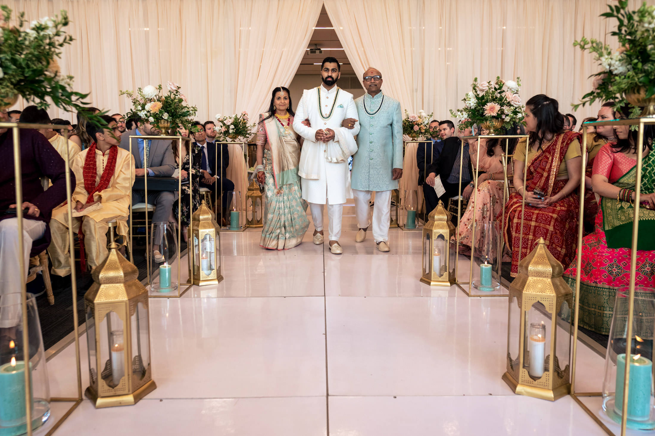 A groom walks down the aisle with two elders at a wedding ceremony.