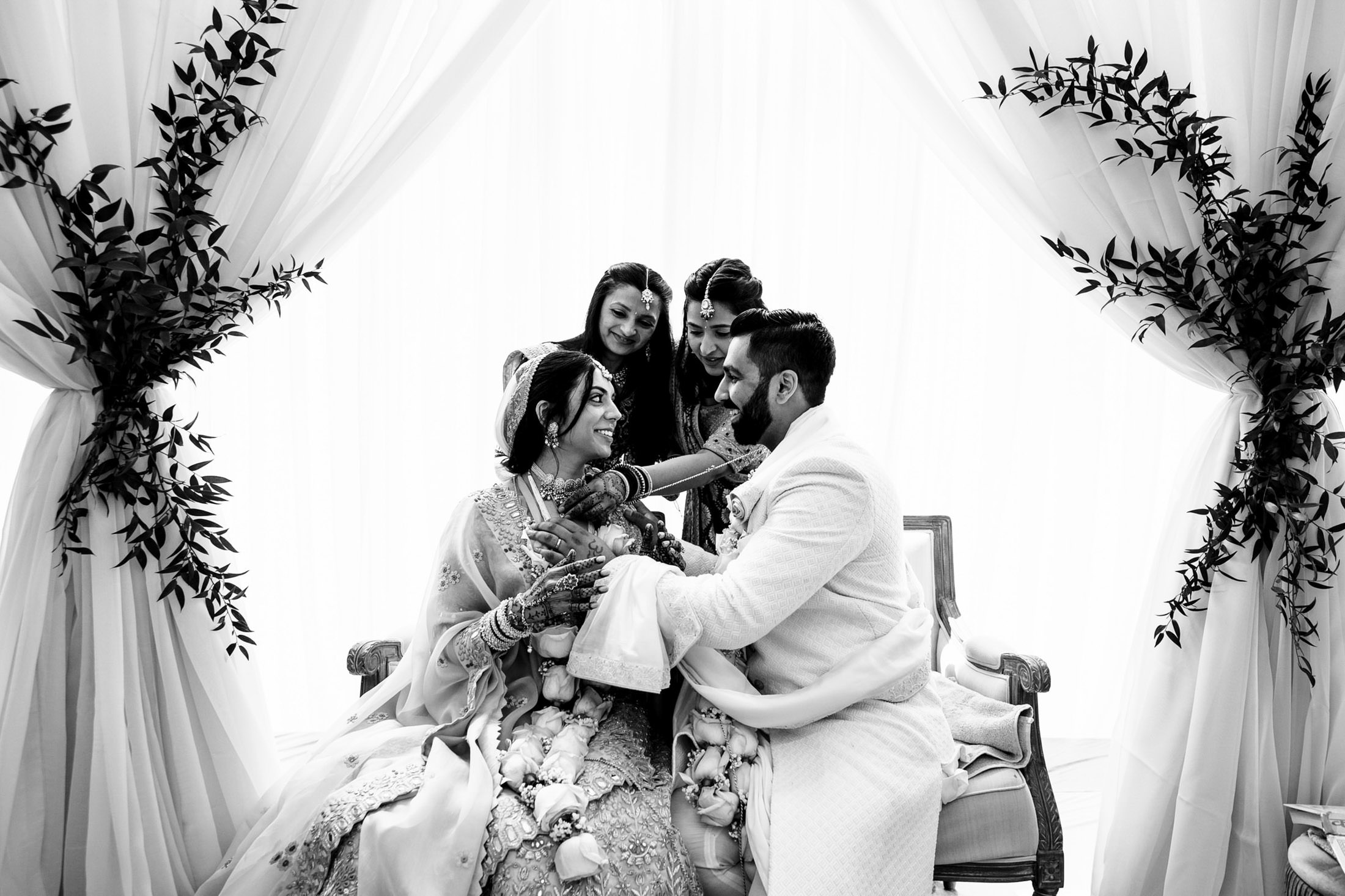 A joyful couple smiling and holding hands, surrounded by two happy friends in elegant attire.