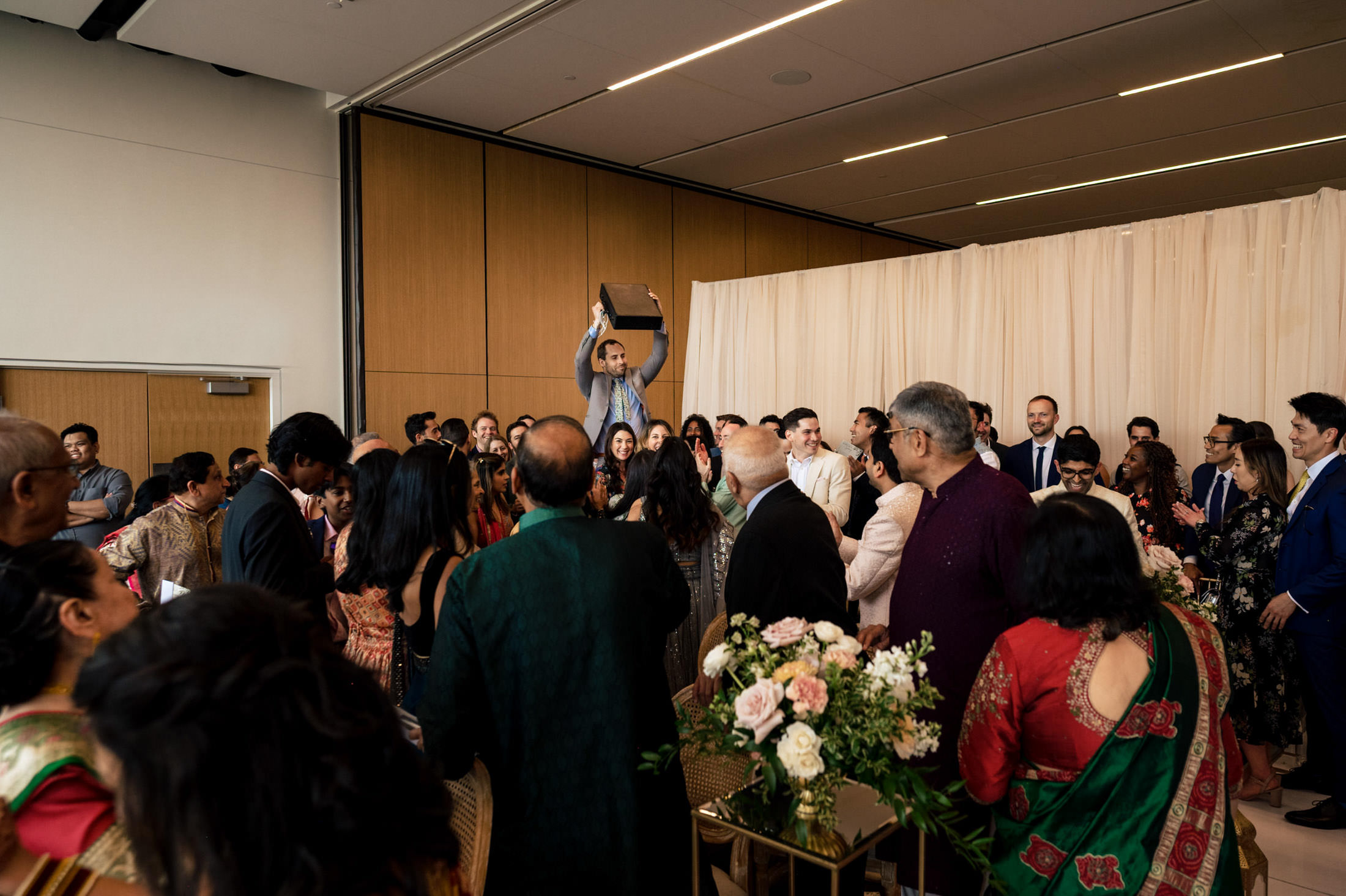 A man holds a box aloft in a crowded indoor gathering.