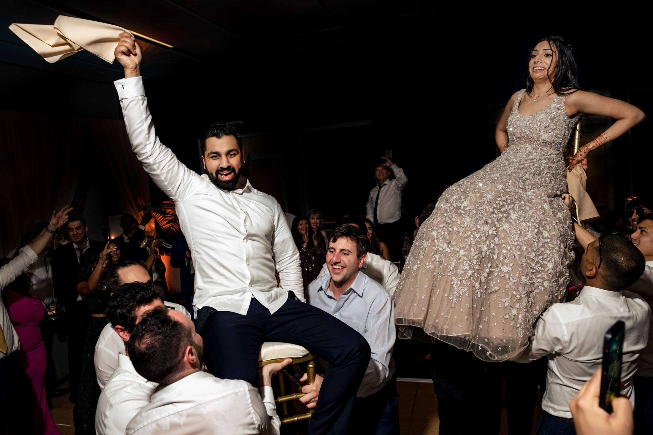 People lift a couple on chairs in a lively celebration at a party.