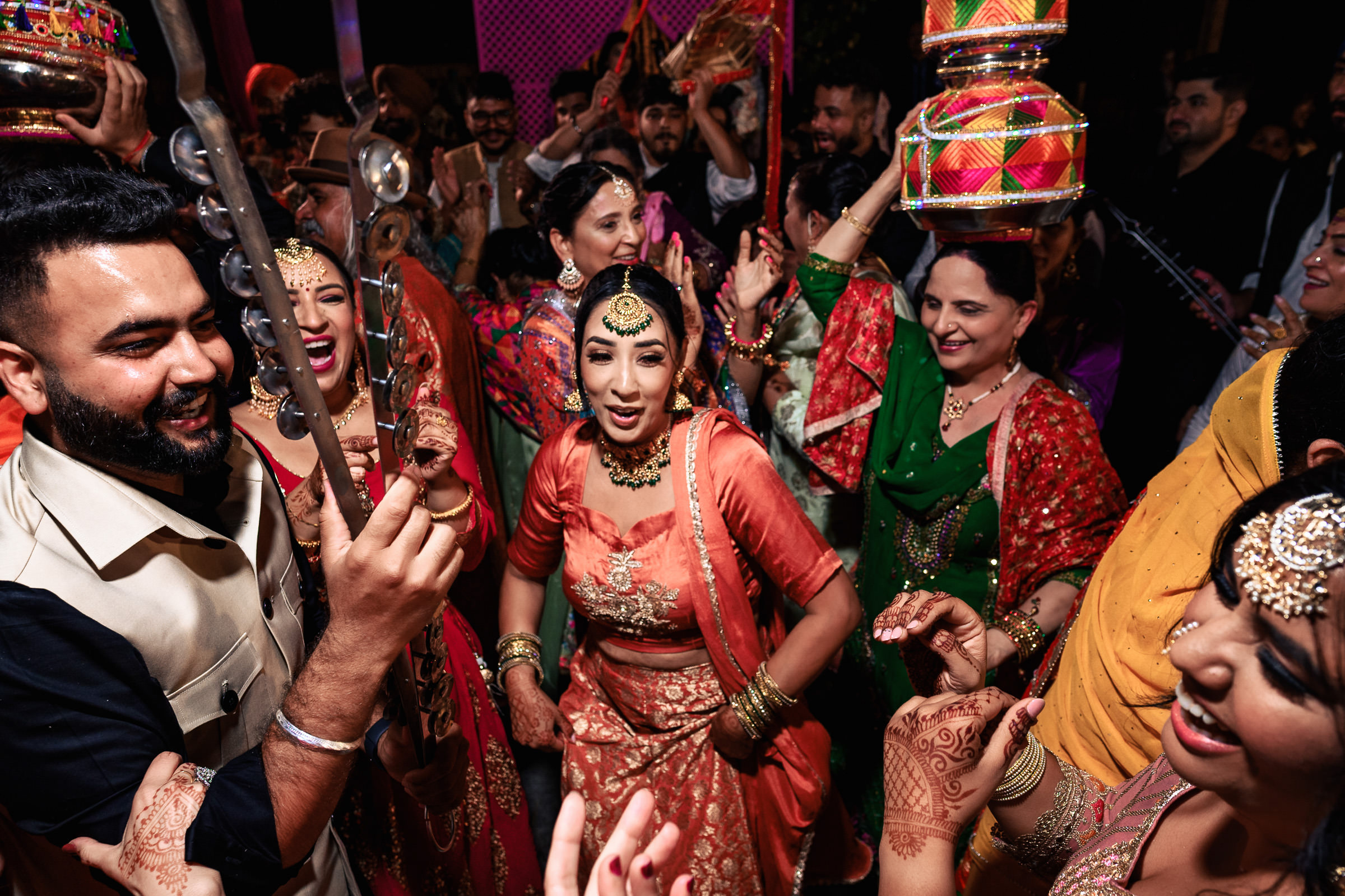 Group of people energetically dancing in colorful attire at an Indian wedding celebration.