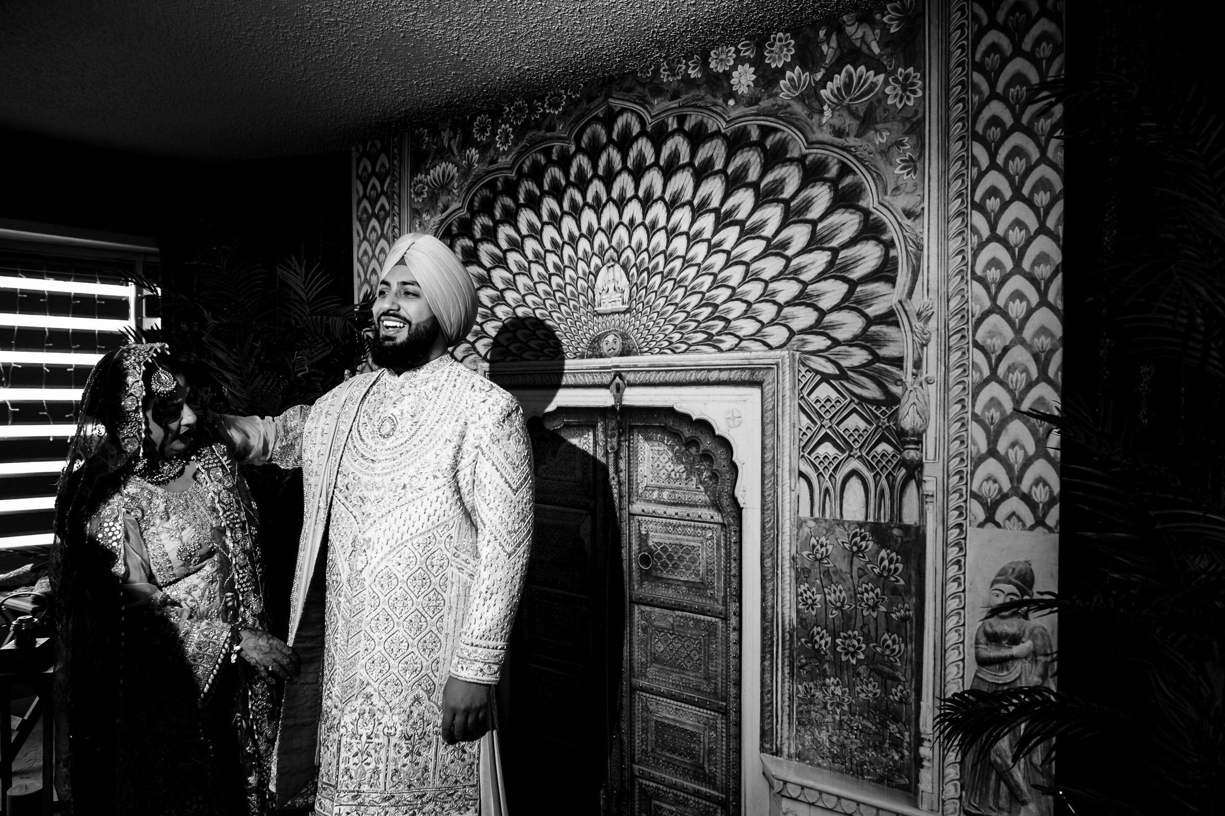 A couple in traditional attire pose for Indian wedding photography against an ornate wall.