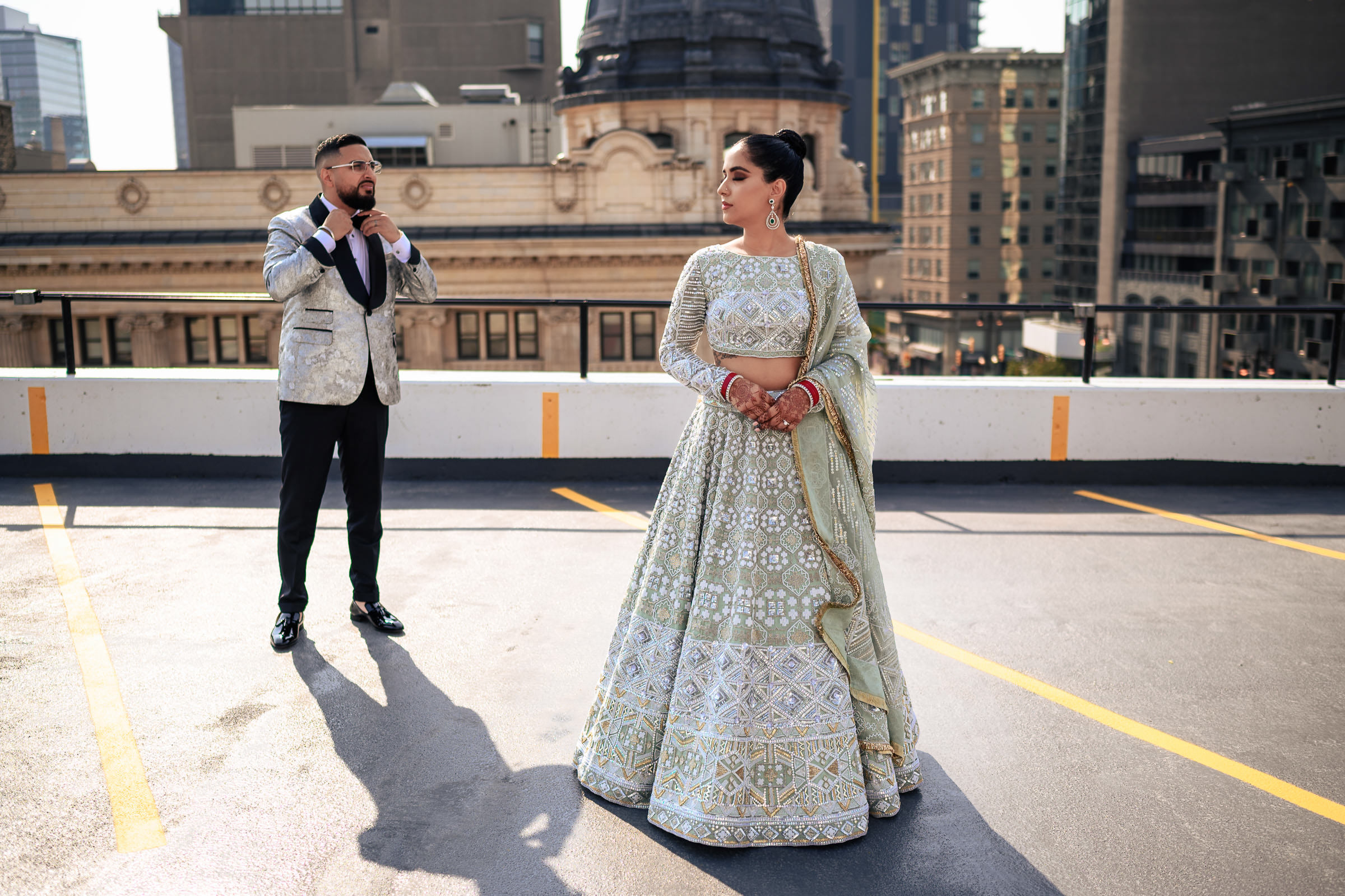 A couple in Indian wedding attire on a rooftop with city buildings in the background.