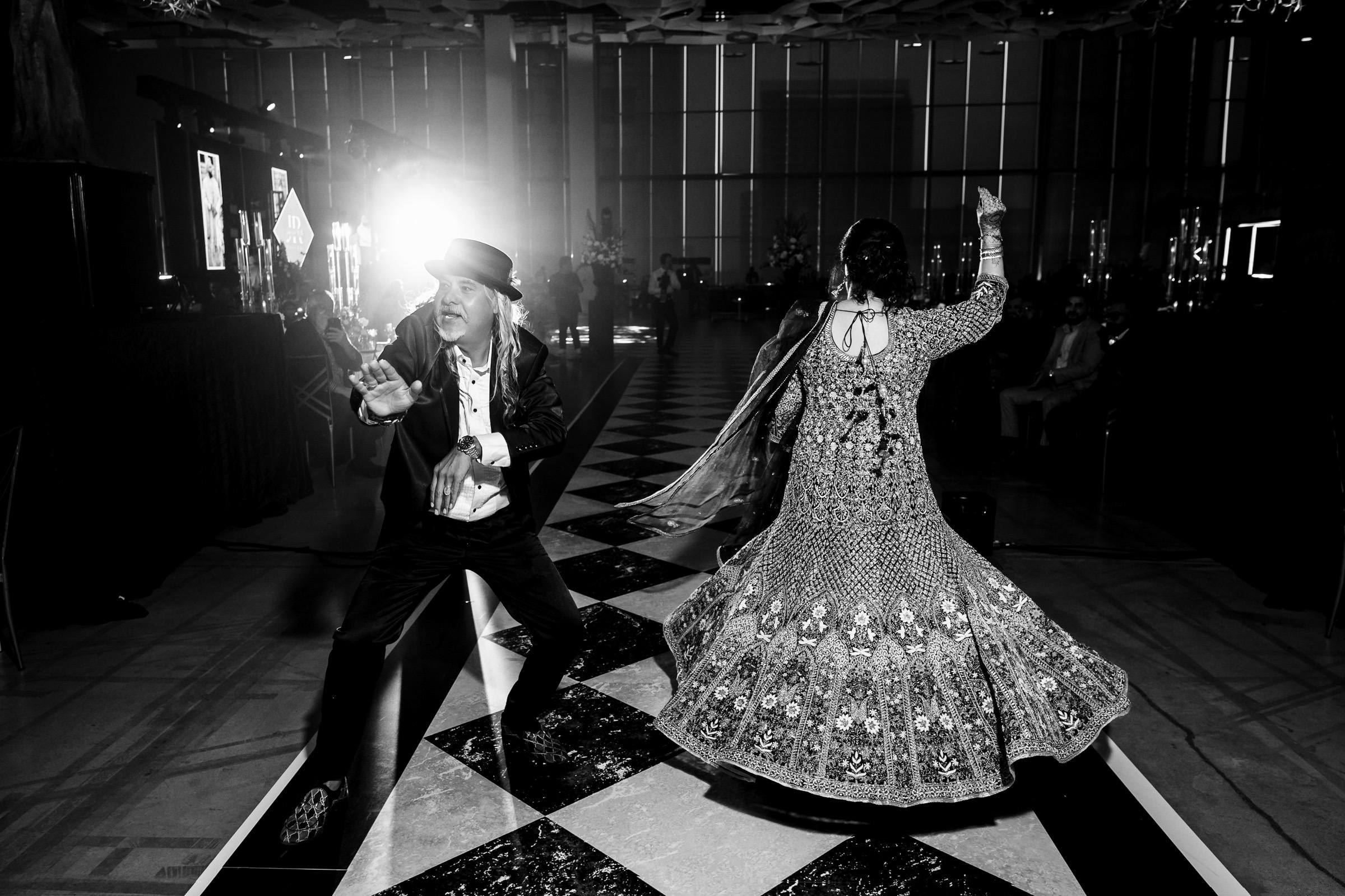 Two people dancing energetically on a checkered floor at an Indian wedding party.