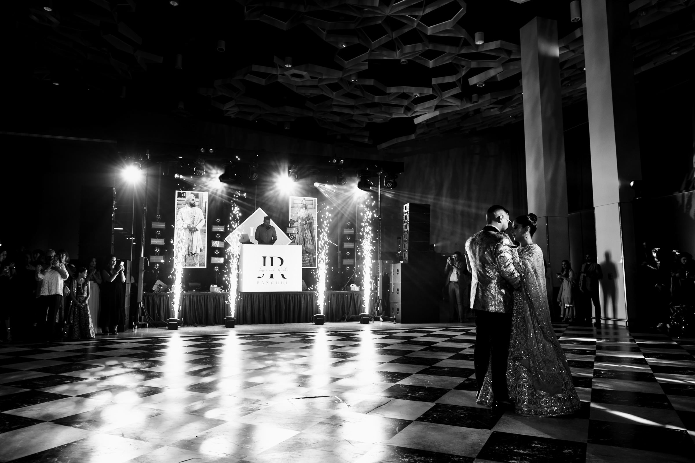 Couple dancing at a grand Indian wedding with a DJ and light effects in a spacious venue.