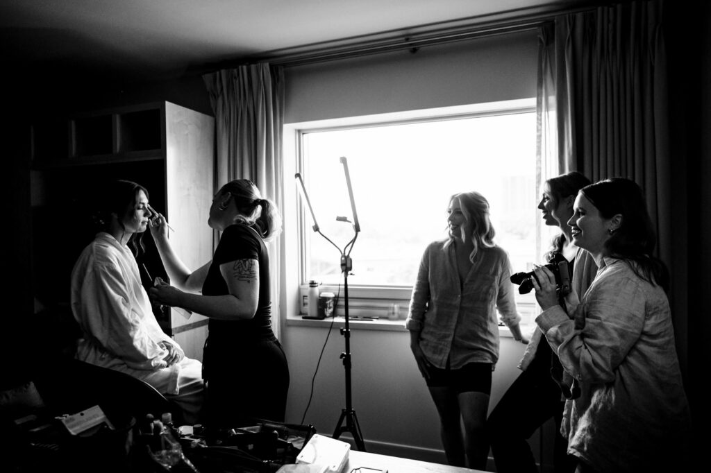 A group of people having fun in a room while one person gets makeup done.