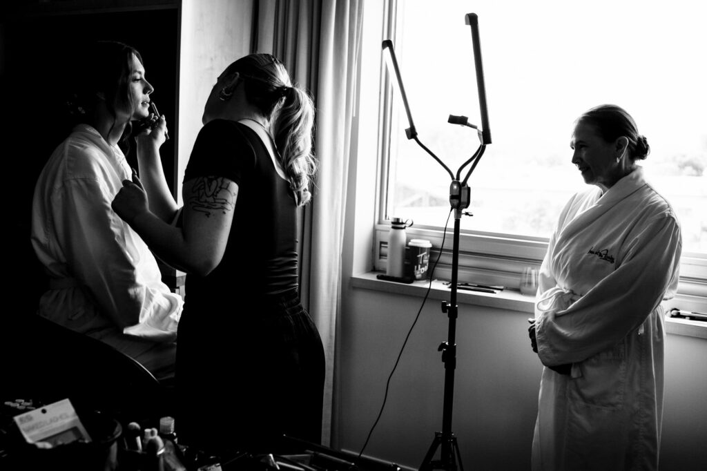 Two women in robes getting makeup done near a window; black and white photo.