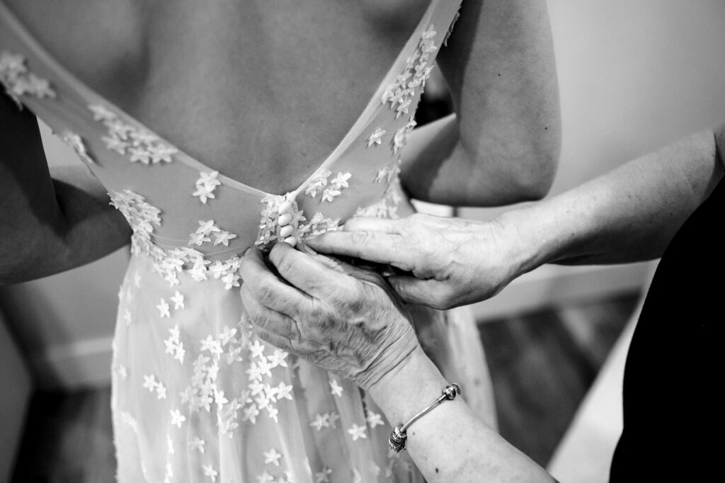 Hands buttoning the back of a lace wedding dress adorned with floral patterns.