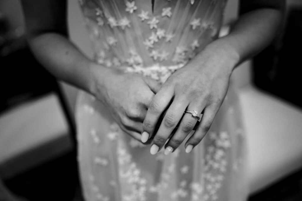 Black and white image of a person in a floral dress showing an engagement ring.