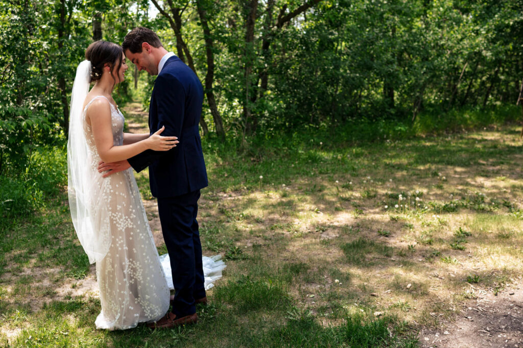 Bride and groom embrace in a sunlit forest clearing, surrounded by lush greenery.