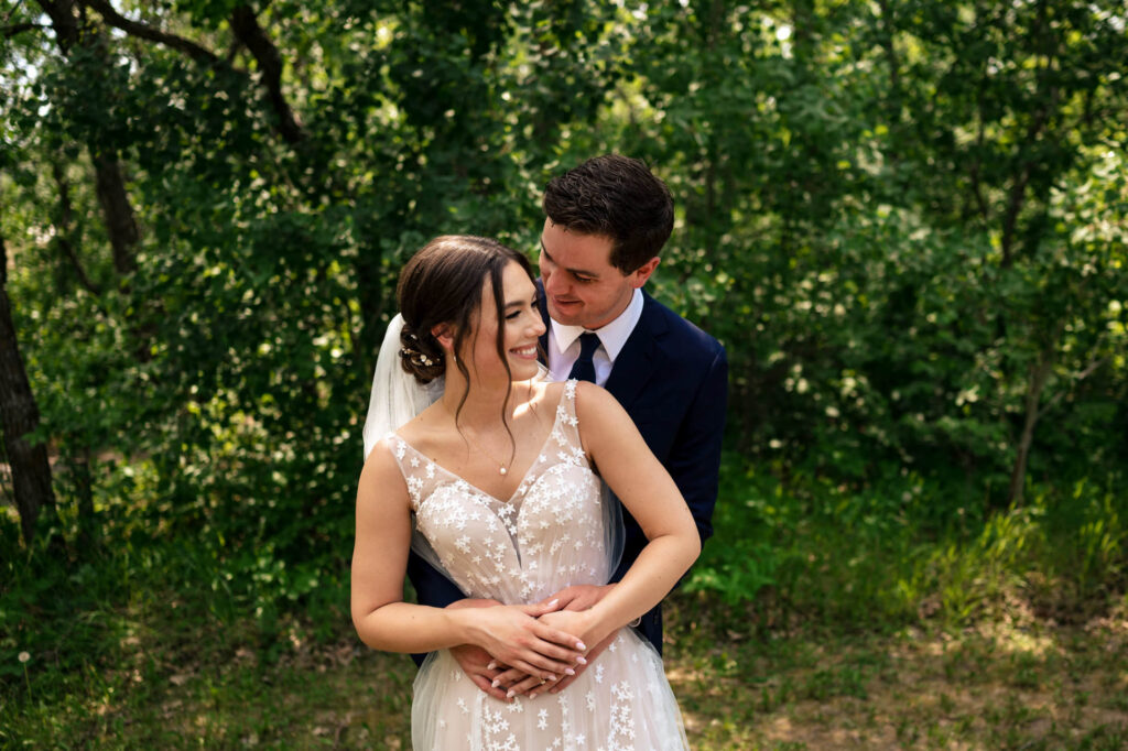 Bride and groom embrace joyfully in a lush green outdoor setting.